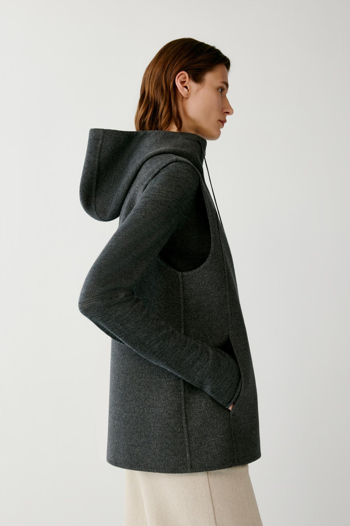 Side view of a woman wearing the dark grey melange sleeveless coat, highlighting the hood and side construction.