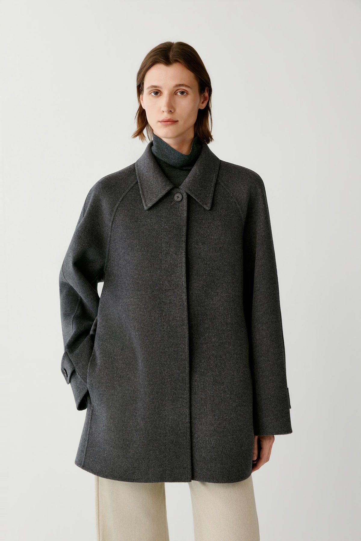 Front view of a woman wearing a dark grey melange wool and cashmere coat, showing the high stand collar, hip-length silhouette and clean construction.