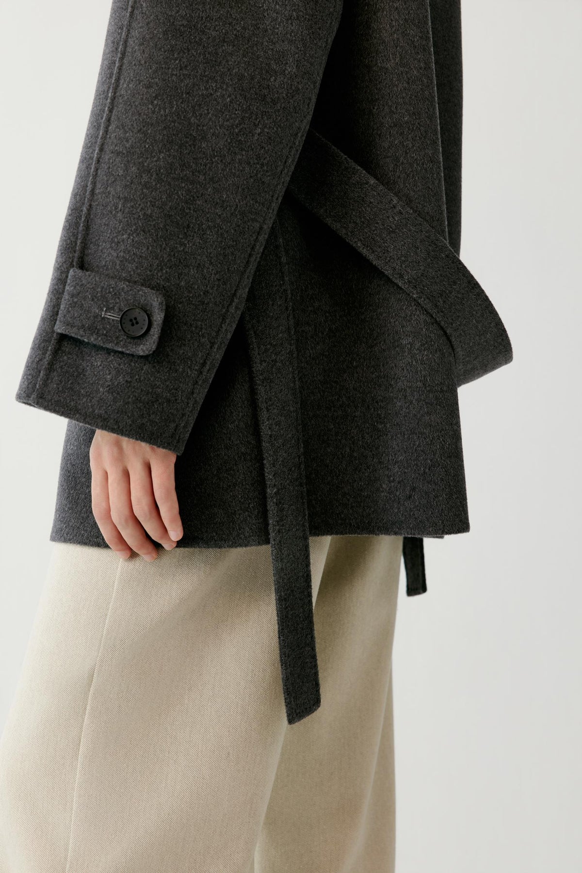 Close-up highlighting the side slit and sleeve of the dark grey melange wool and cashmere coat.