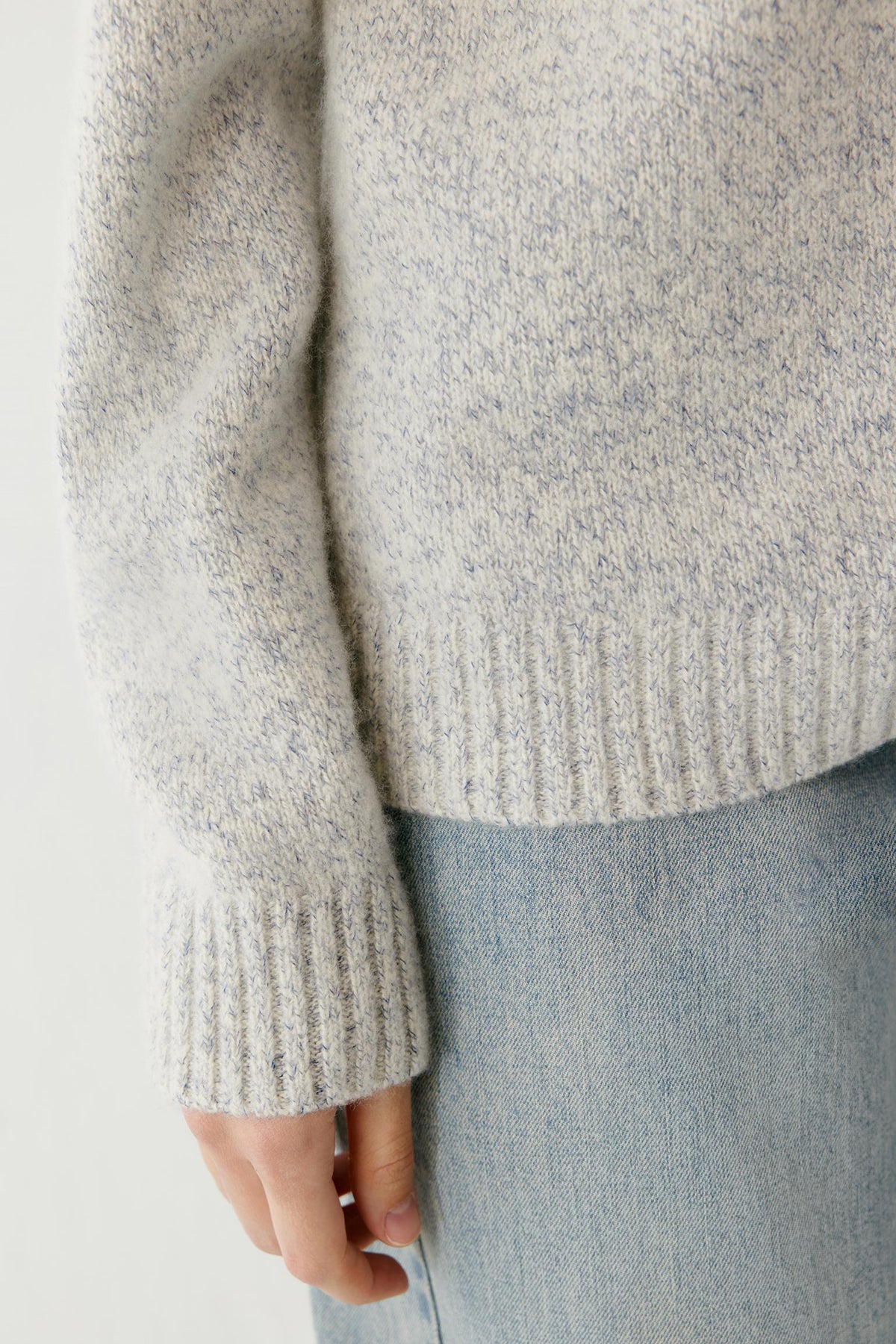 Close-up highlighting the ribbed cuff and blue and white melange texture of the cashmere and silk pullover.