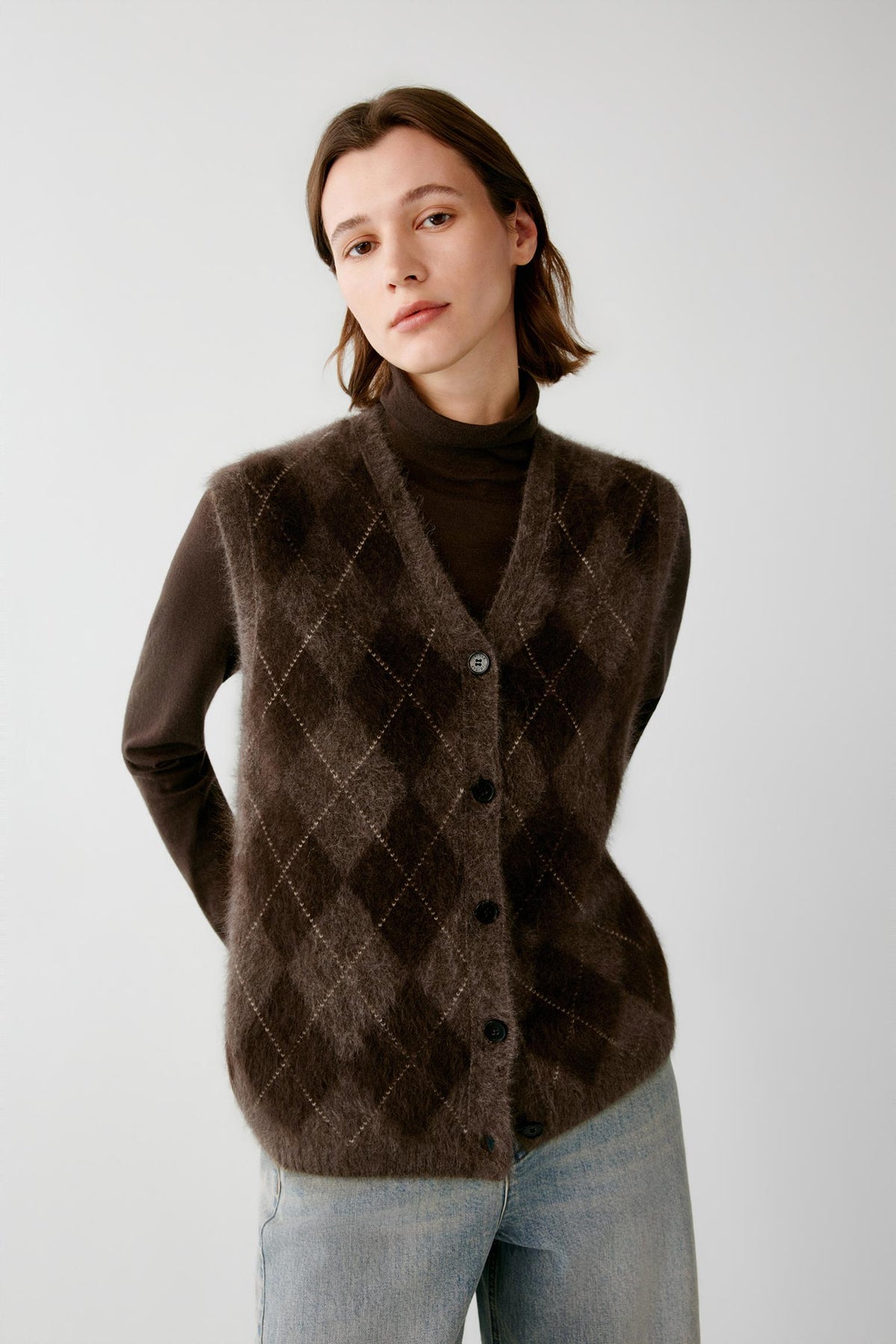 Front view of a woman wearing a dark brown yak sleeveless pullover, showing the V-neckline and contrasting argyle pattern.