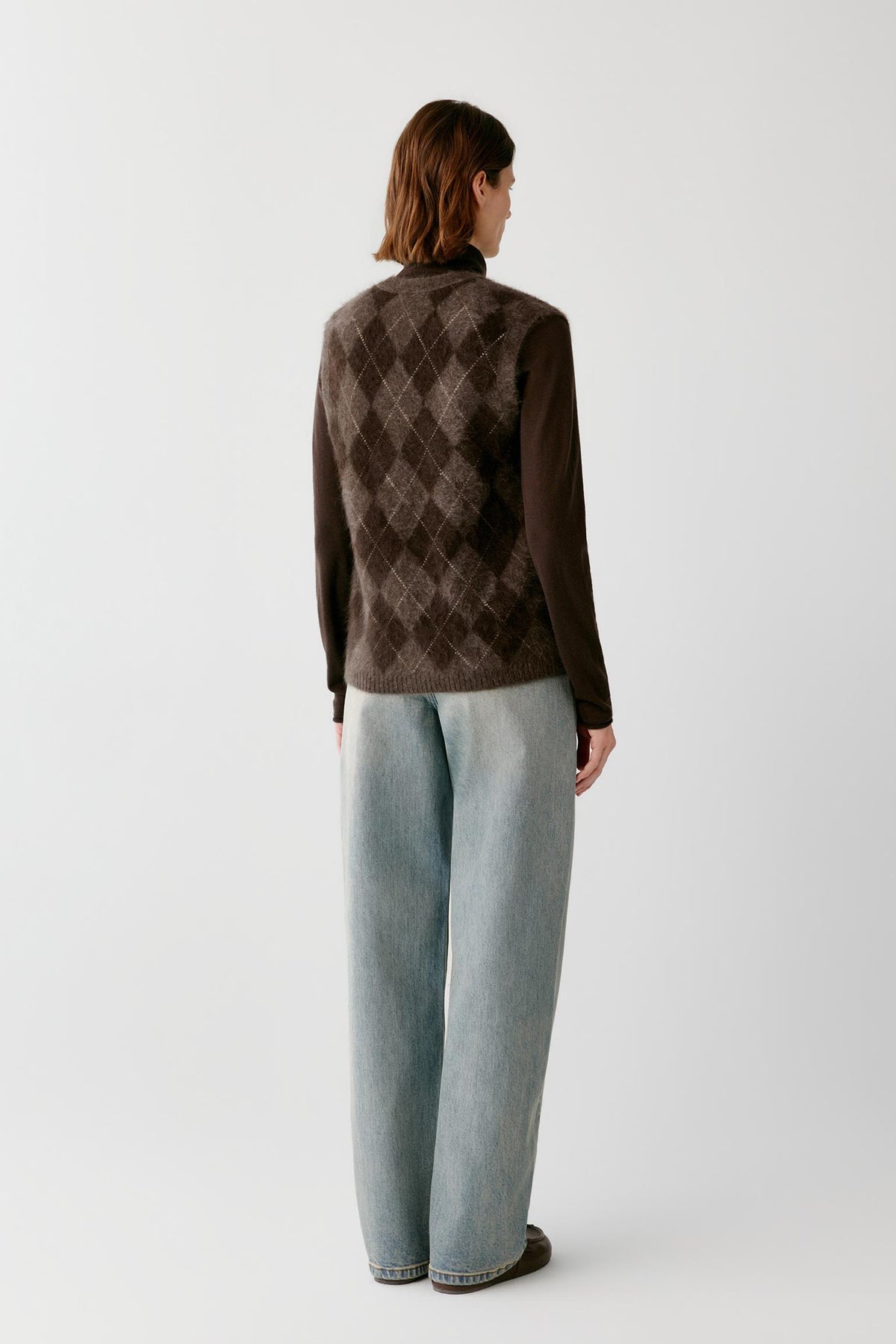 Back view of a woman wearing the dark brown yak sleeveless pullover, showing the argyle pattern and sleeveless construction.
