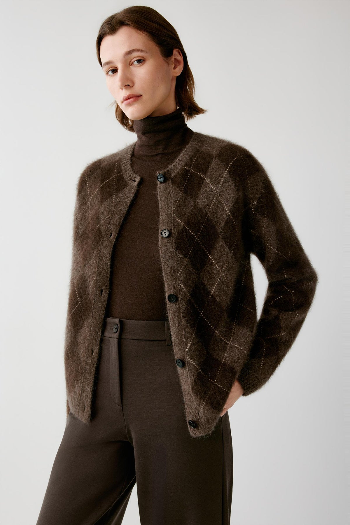 Front view of a woman wearing a dark brown yak cardigan, showing the crew neckline, button-front fastening and contrasting argyle pattern.