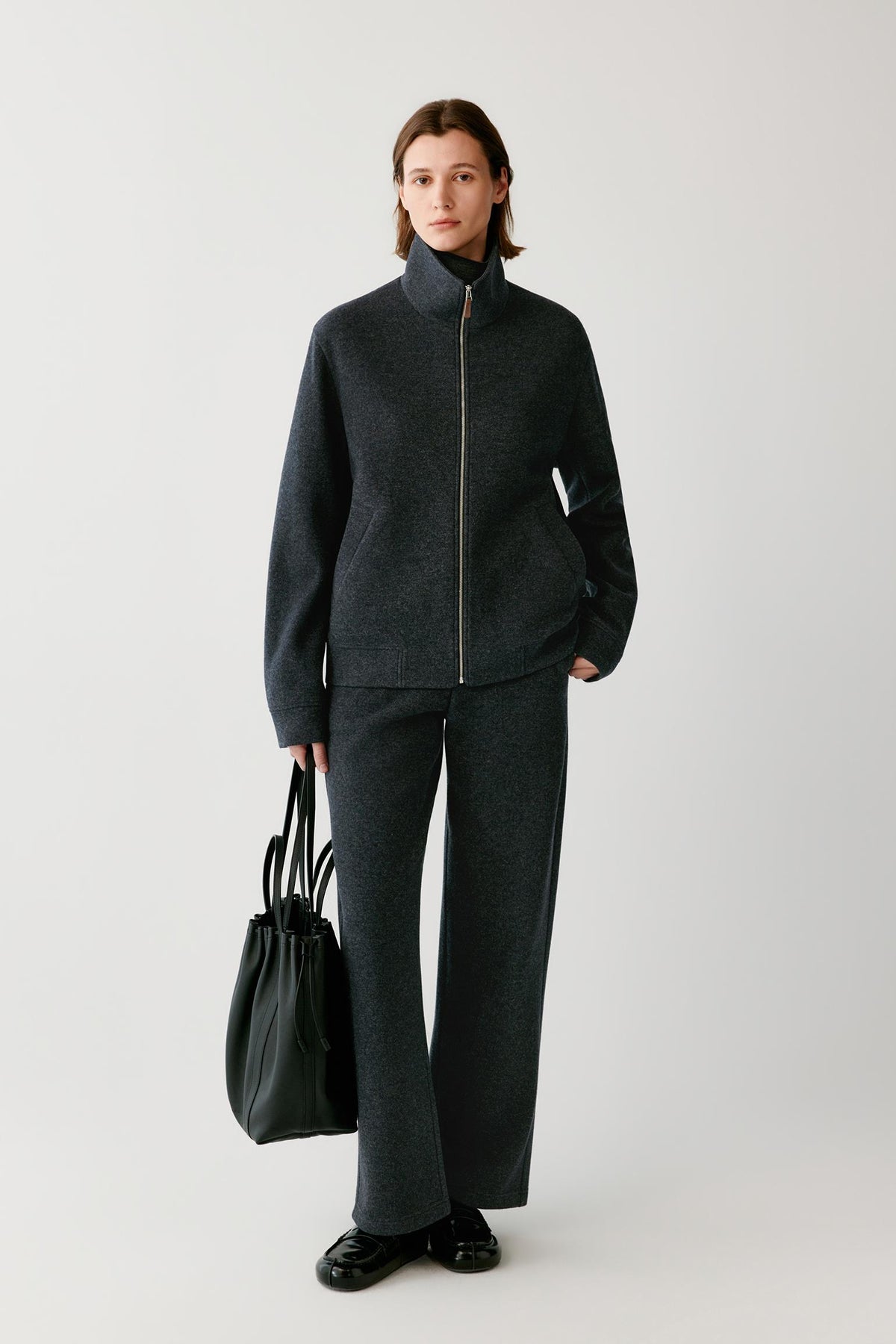 Front view of a woman wearing a grey melange wool and cashmere jersey blouson, showing the stand collar, zip front and welt pockets.