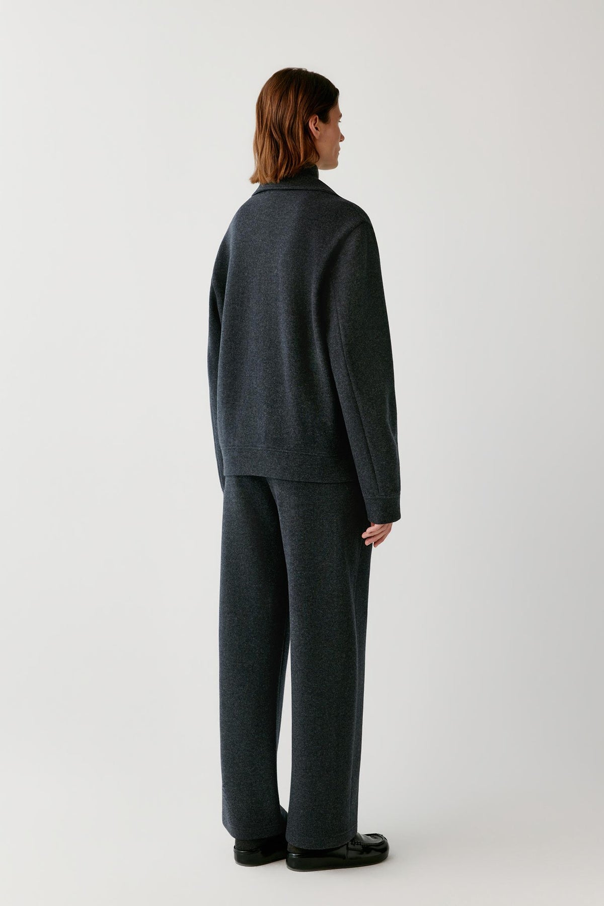 Back view of a woman wearing the grey melange wool and cashmere jersey blouson, showing the straight silhouette and long sleeves.