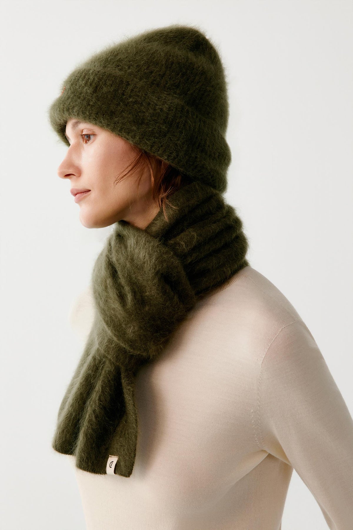Side view of a woman wearing the dark green brushed cashmere beanie, highlighting the turned-up cuff, rounded crown and brushed texture.