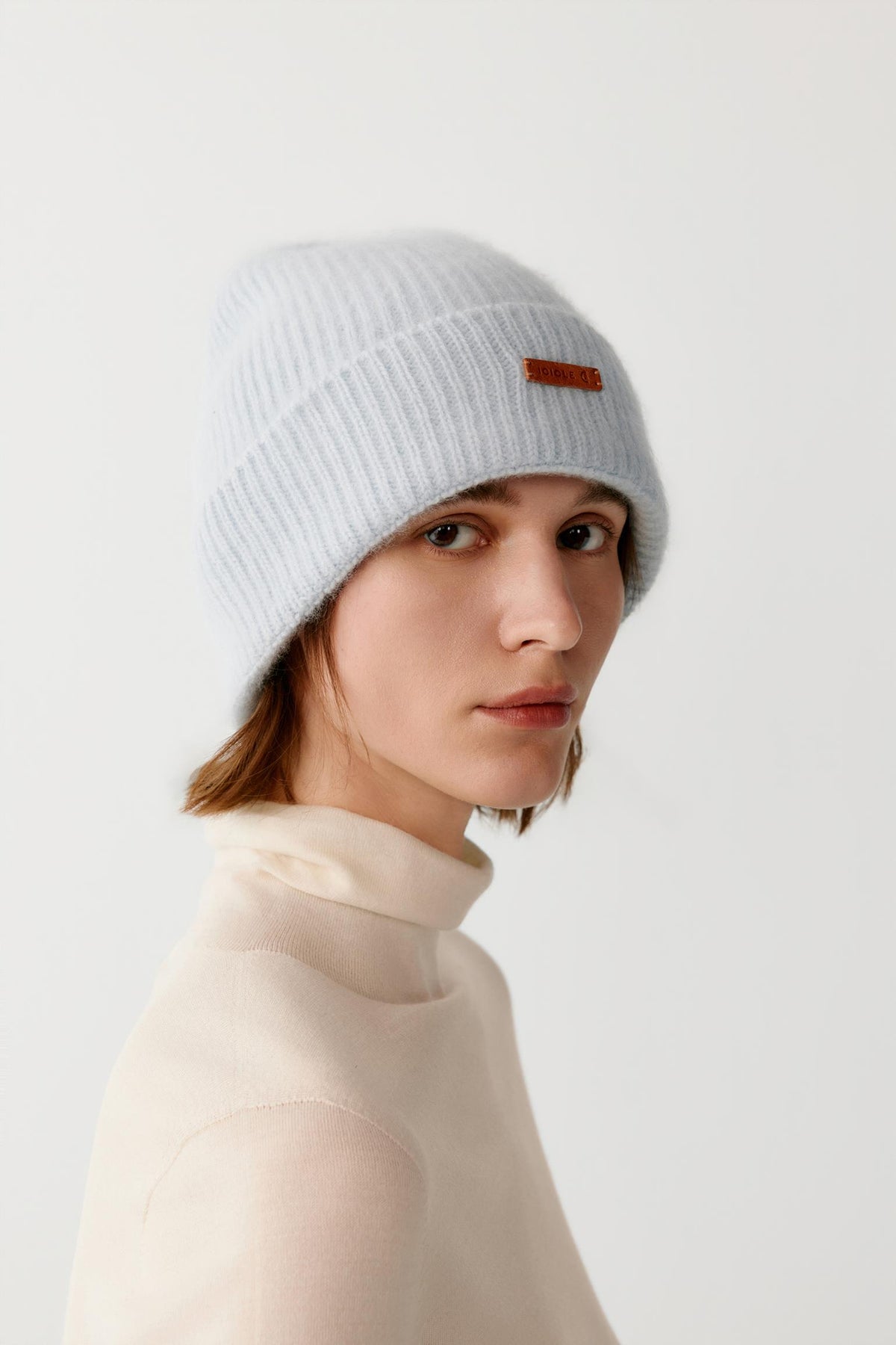 Three-quarter view of a woman wearing the light blue brushed cashmere beanie, showing the rounded crown and ribbed turned-up cuff.