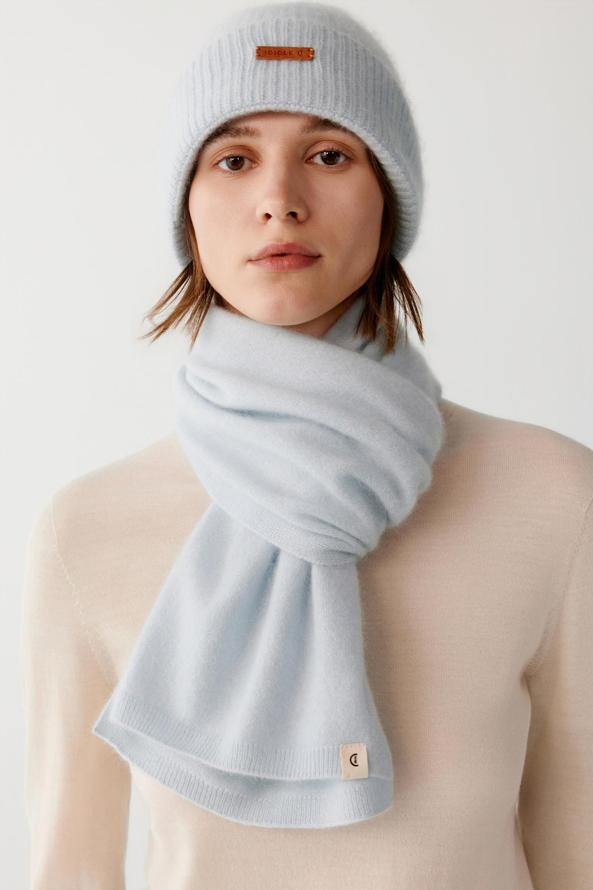 Front view of a woman wearing a light blue brushed cashmere scarf wrapped around the neck, showing the long ends and brushed texture.