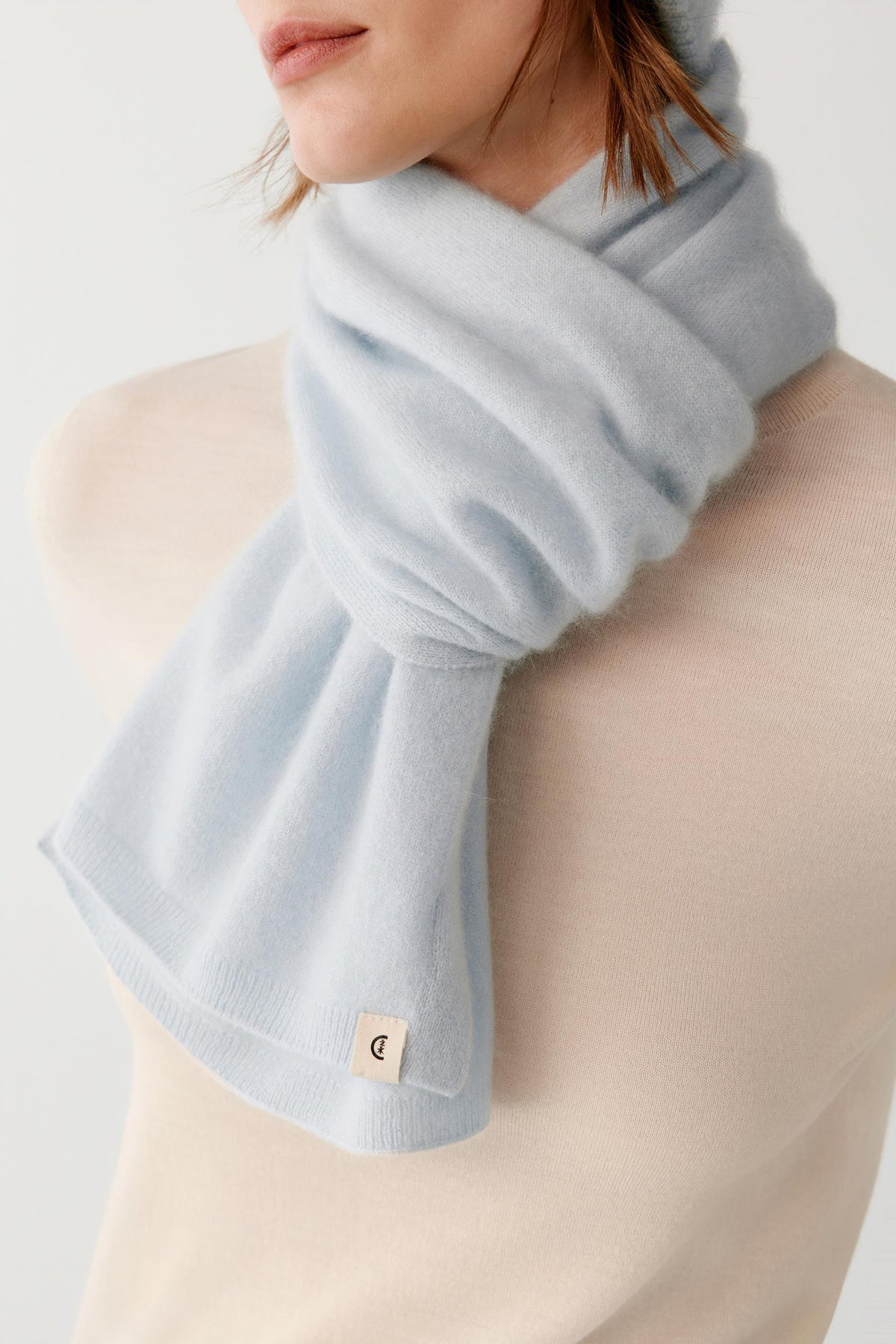 Close-up highlighting the light blue brushed cashmere scarf wrapped around the neck, showing its soft textured surface and drape.