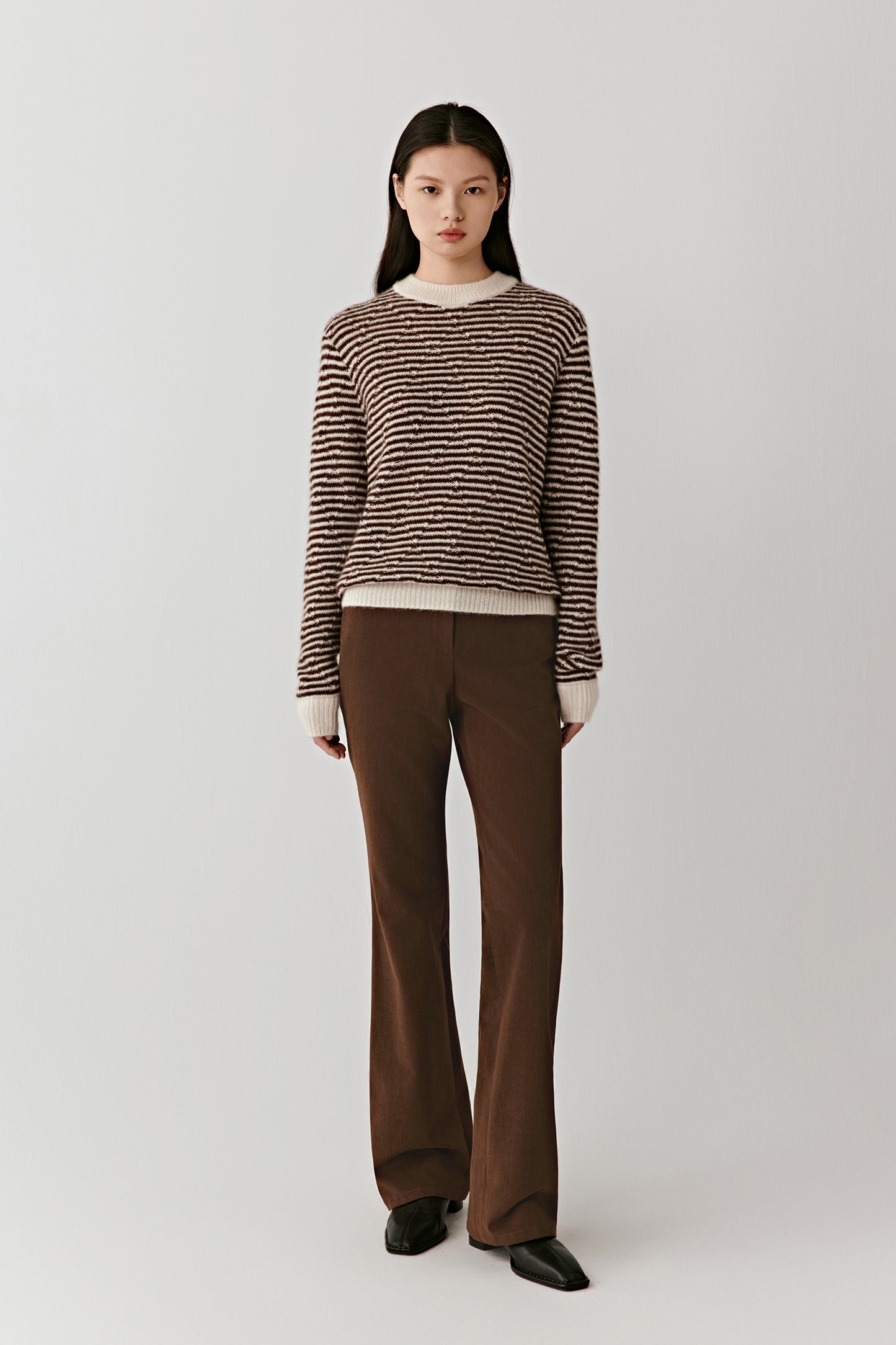 Full-length view of a person wearing a brown and off-white striped cashmere-silk pullover paired with brown trousers, standing against a light background.