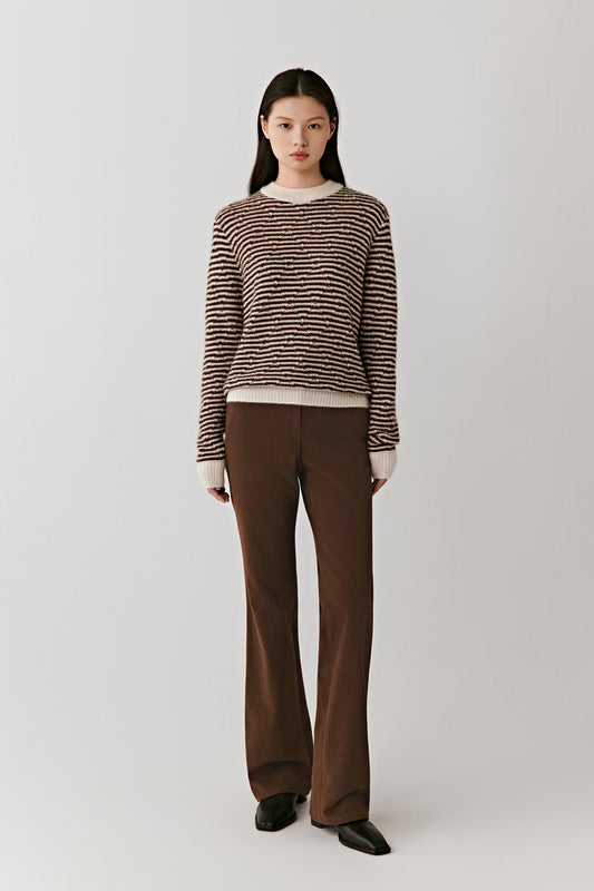 Full-length view of a person wearing a brown and off-white striped cashmere-silk pullover paired with brown trousers, standing against a light background.
