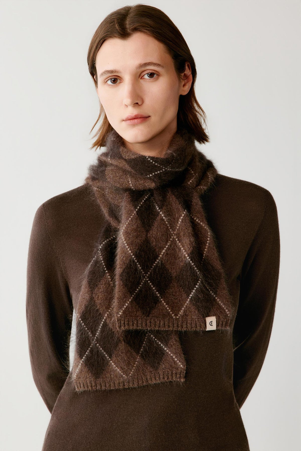 Front close-up of a woman wearing the dark brown brushed cashmere scarf, highlighting the argyle pattern and ribbed edges.