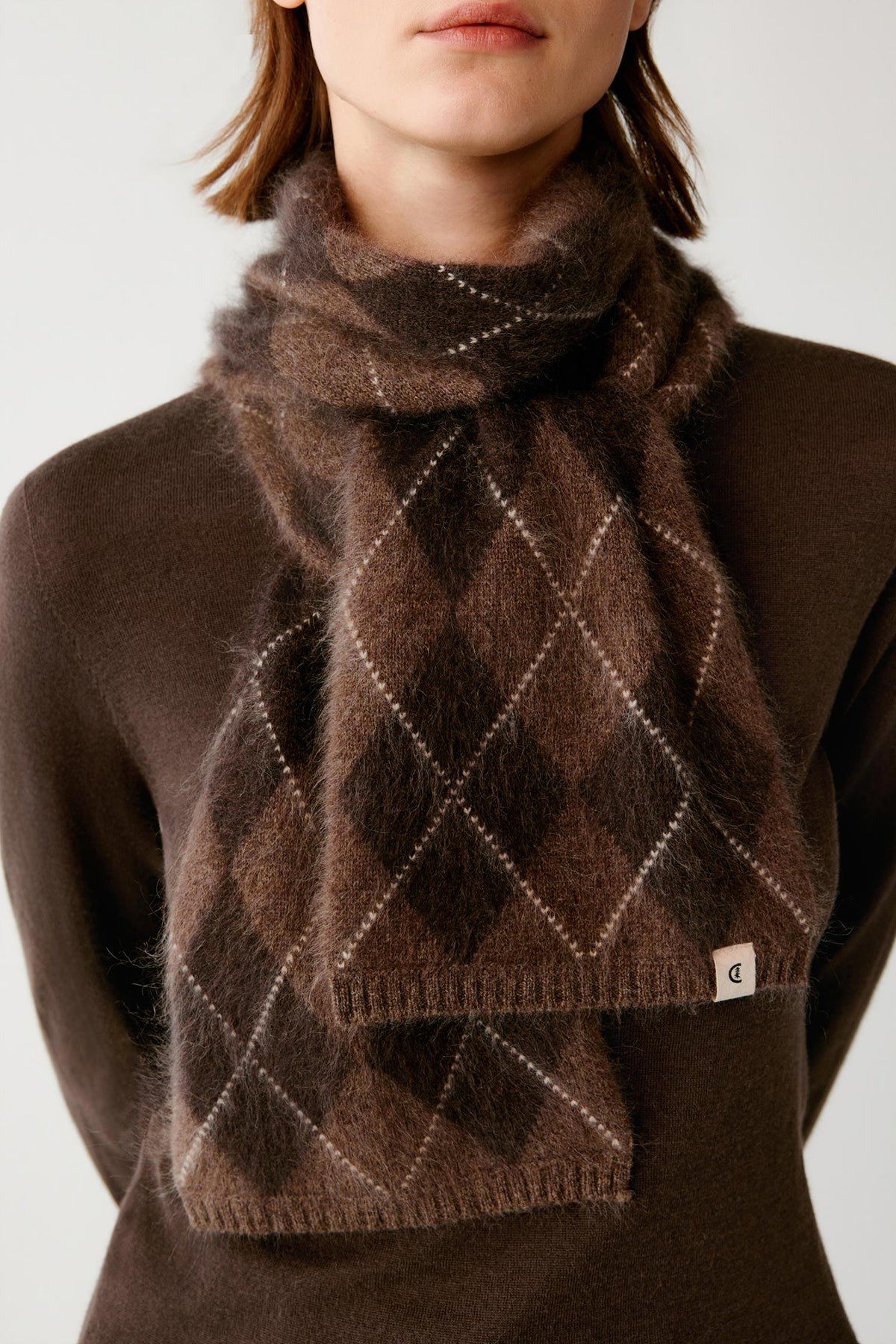 Close-up highlighting the contrasting argyle pattern, ribbed edges and brushed texture of the dark brown cashmere scarf.