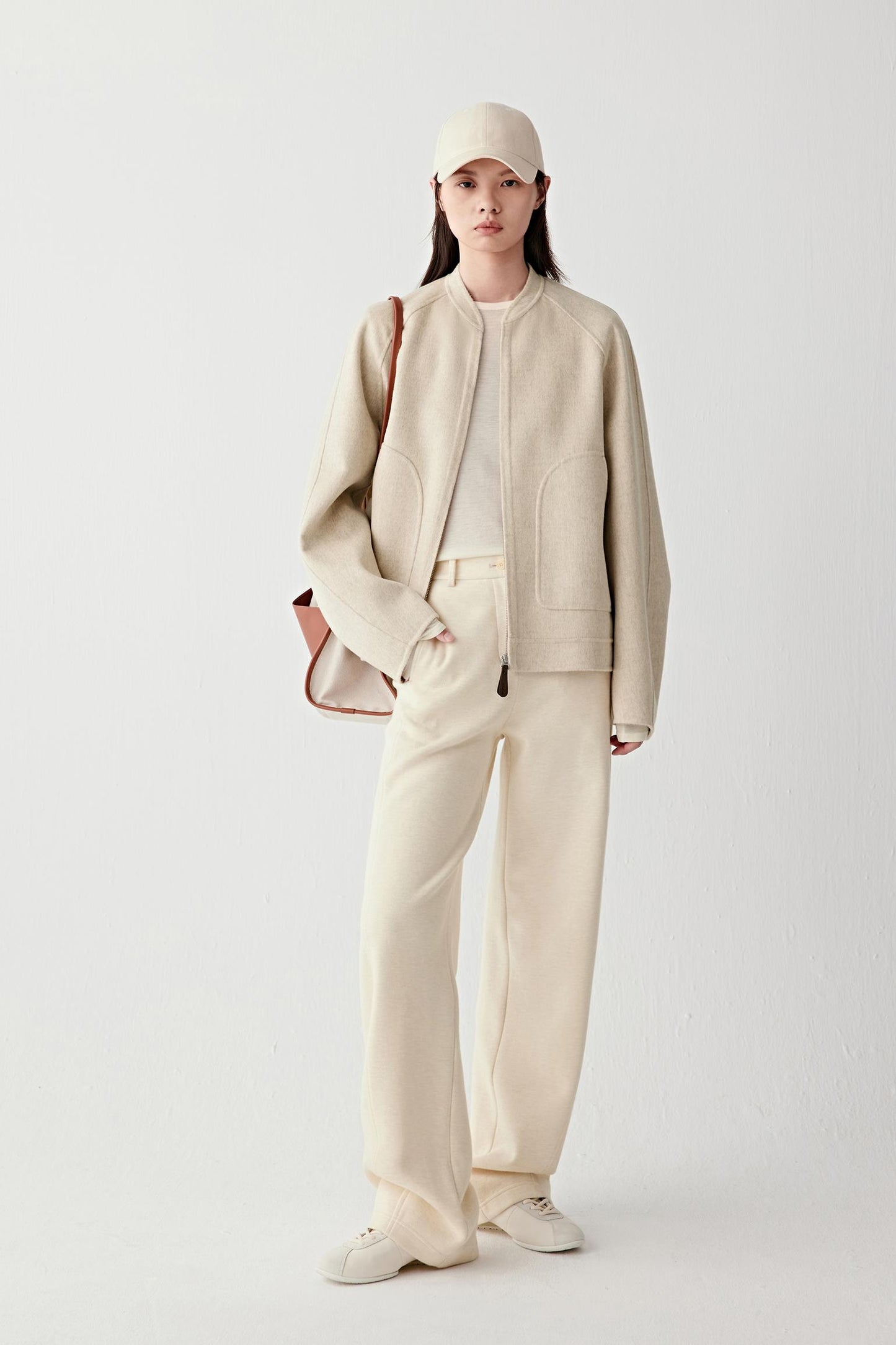 Full-length front view of a beige double-faced wool and cashmere jacket with a relaxed fit, collarless neckline and straight hem, worn with matching trousers.