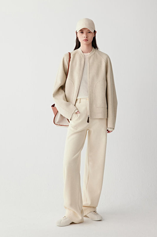Full-length front view of a beige double-faced wool and cashmere jacket with a relaxed fit, collarless neckline and straight hem, worn with matching trousers.