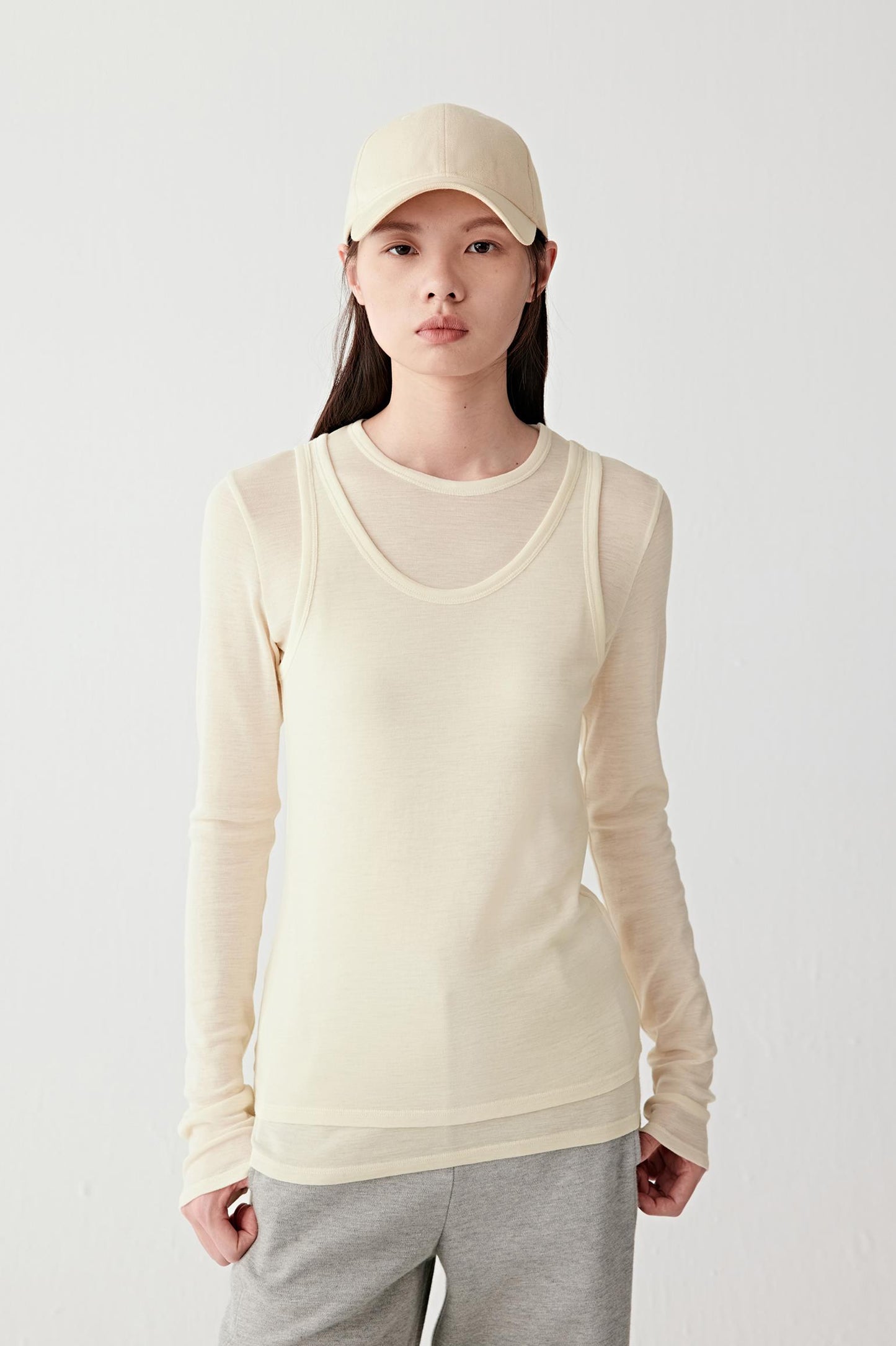 Person wearing a beige long-sleeve top and cap on a white background
