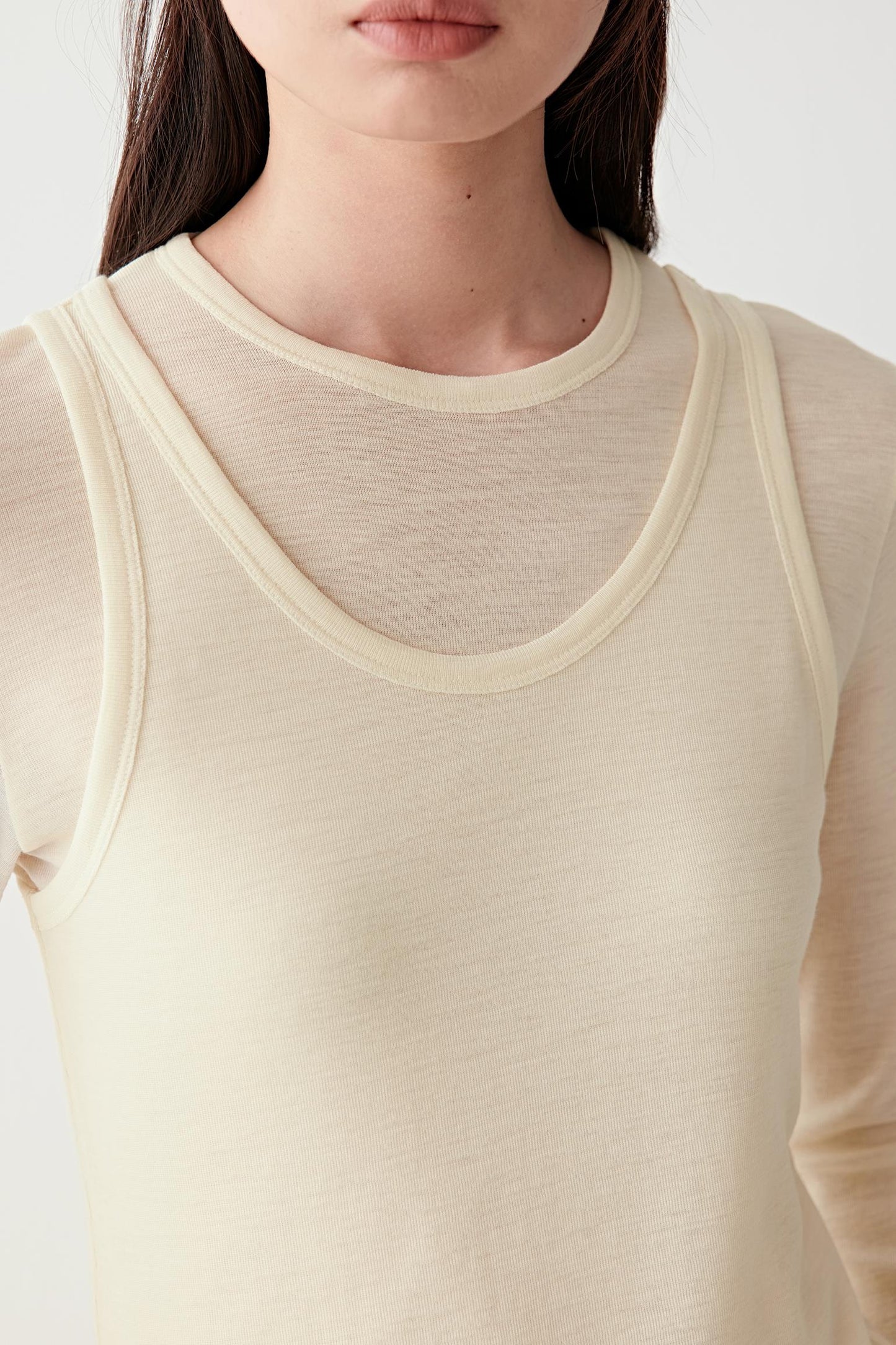 Close-up of a person wearing a beige long-sleeve shirt against a white background