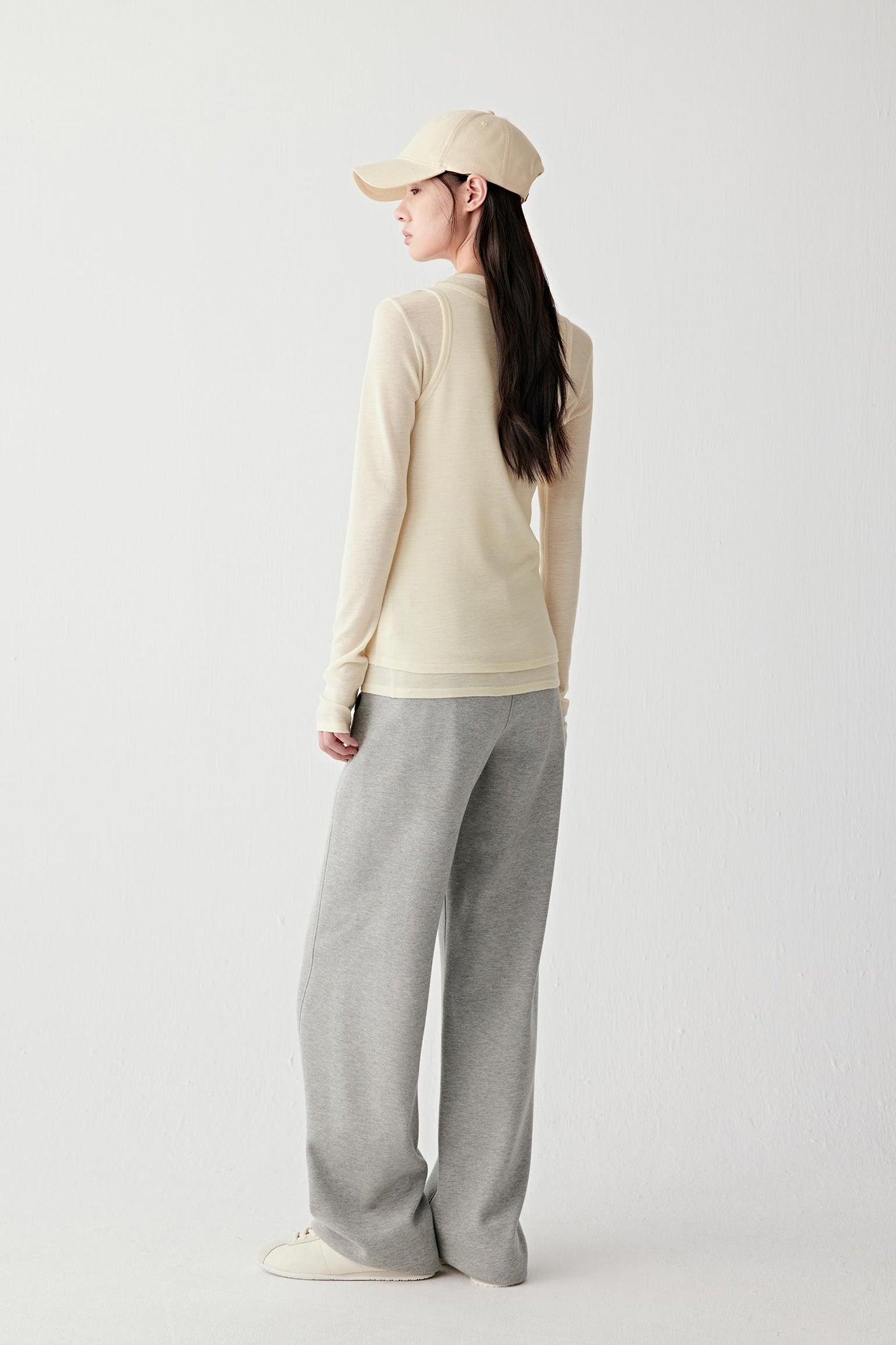 Person wearing a beige sweater and gray pants on a white background