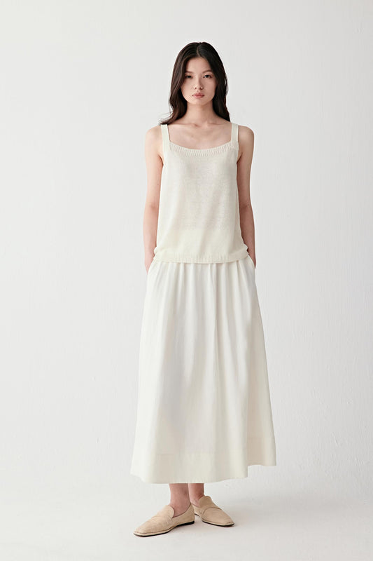 Full-length front view of a woman wearing a long off-white silk linen skirt with a gathered elastic waistband, showing soft volume, airy structure and fluid drape to the ankles, styled with a sleeveless top