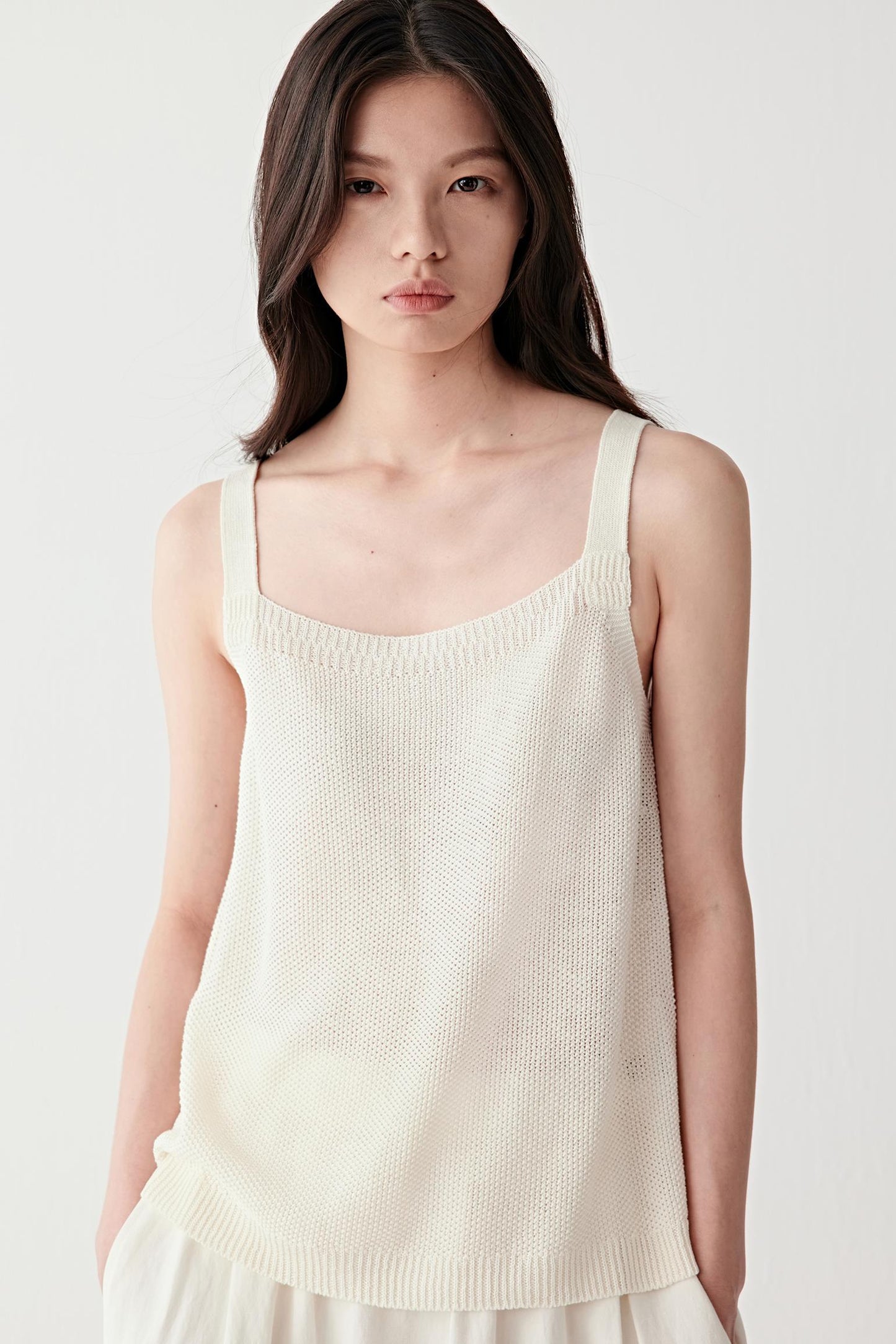 Front close-up view of a woman wearing a light cream linen-silk tank top with a fine knit structure, thin straps and soft square neckline, highlighting smooth texture and lightweight construction