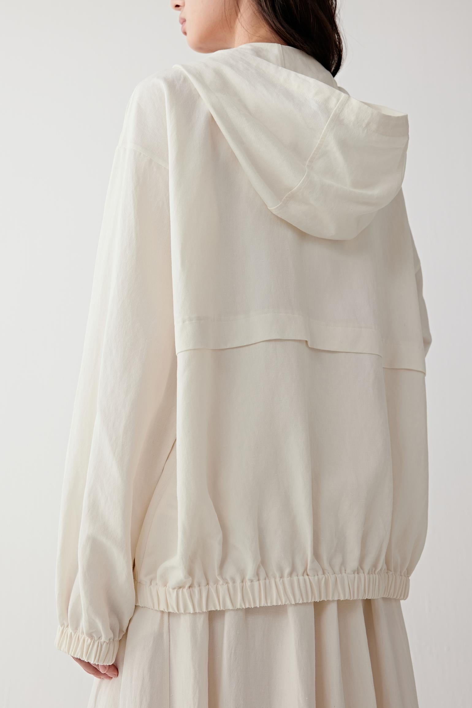 Back view showing the hood shape, the straight fall from shoulders to hem and the gathered hemline, emphasizing the balance between structure and softness