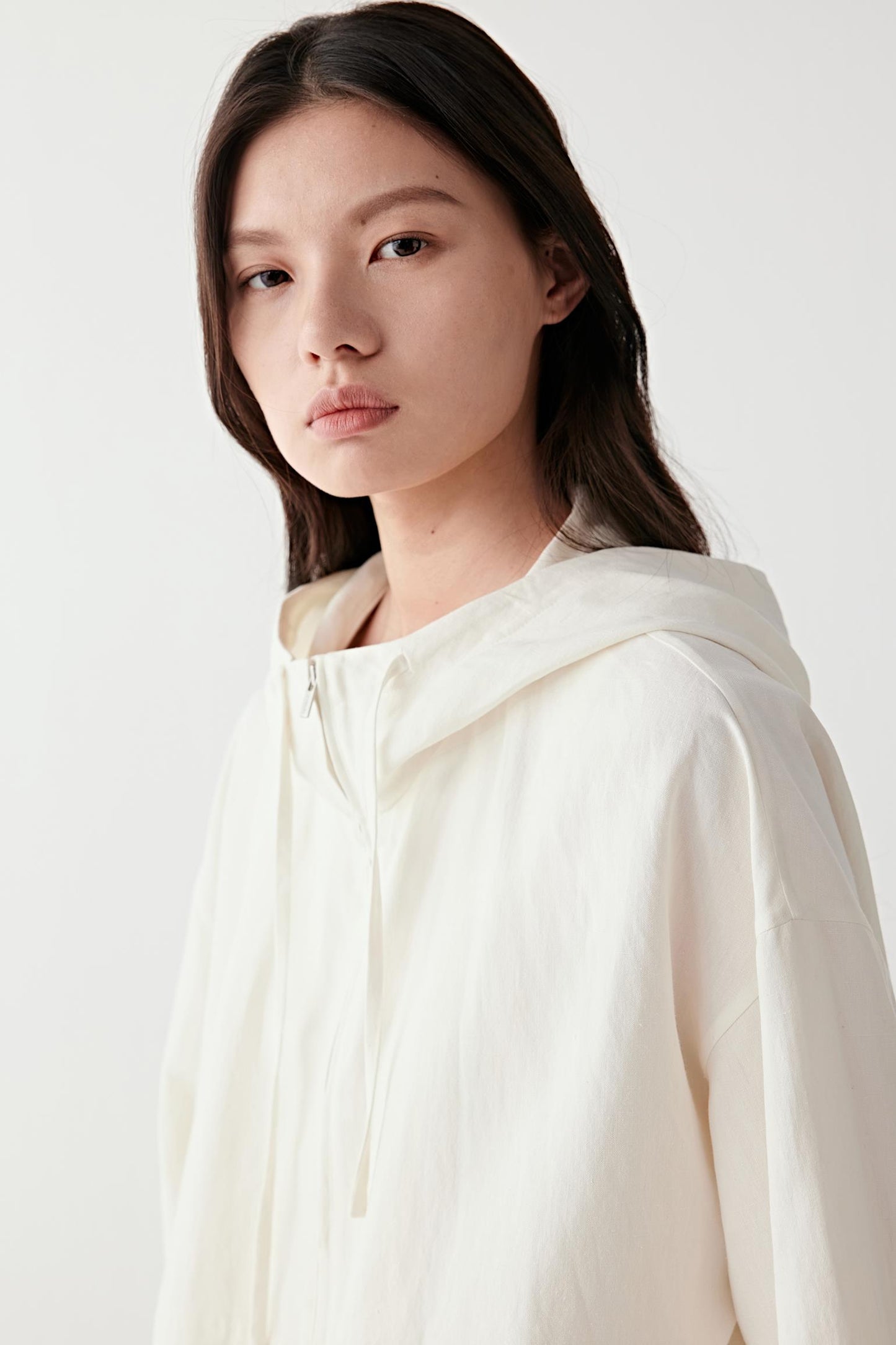 Close-up portrait focusing on the hood and neckline, highlighting the construction of the hood, the clean edges and the lightly textured, matte surface of the fabric