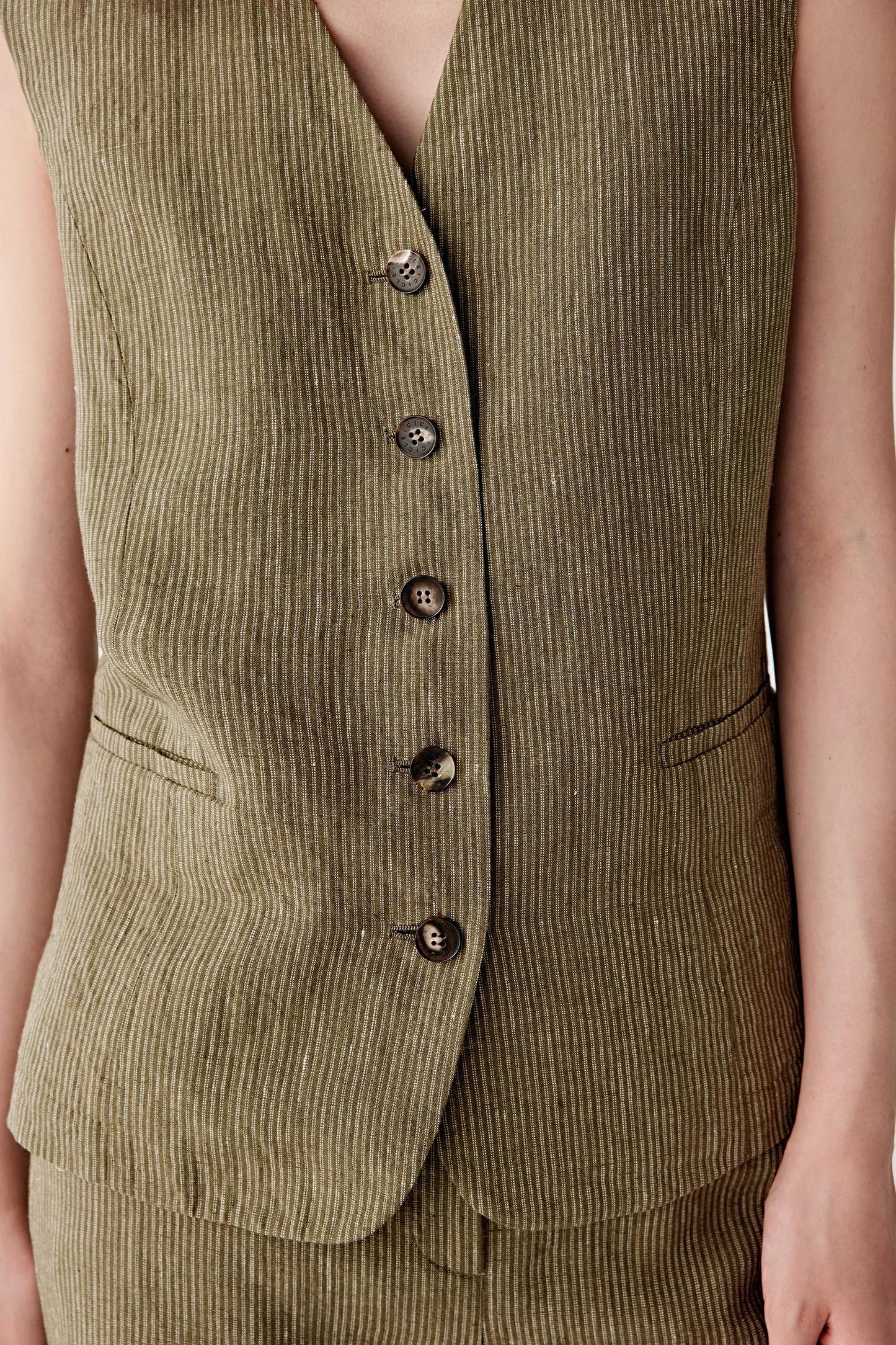 Close-up of the front panel focusing on the V neckline, tonal button fastening and the vertical striped pattern, showing stitching details and the slightly irregular texture of yarn-dyed linen