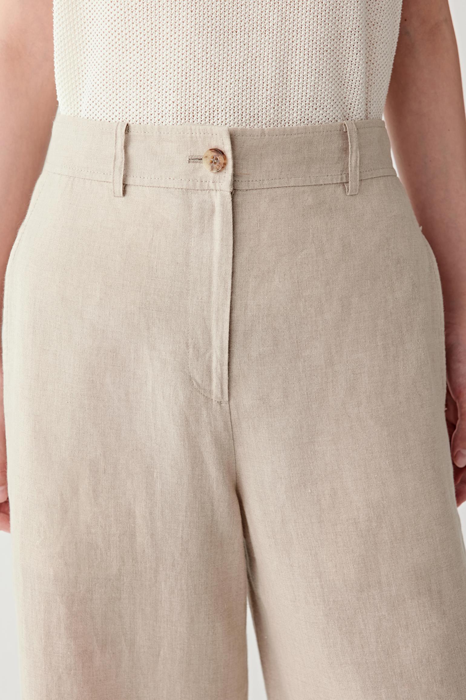 Close-up of waistband and pleats detailing the button fastening, front pleats and belt loops, highlighting the natural irregularities of the linen weave