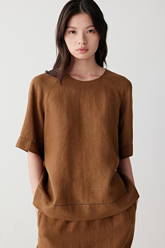 Front view of a woman wearing a brown linen top with a relaxed silhouette, highlighting the lightly textured woven surface, fluid drape and soft matte finish
