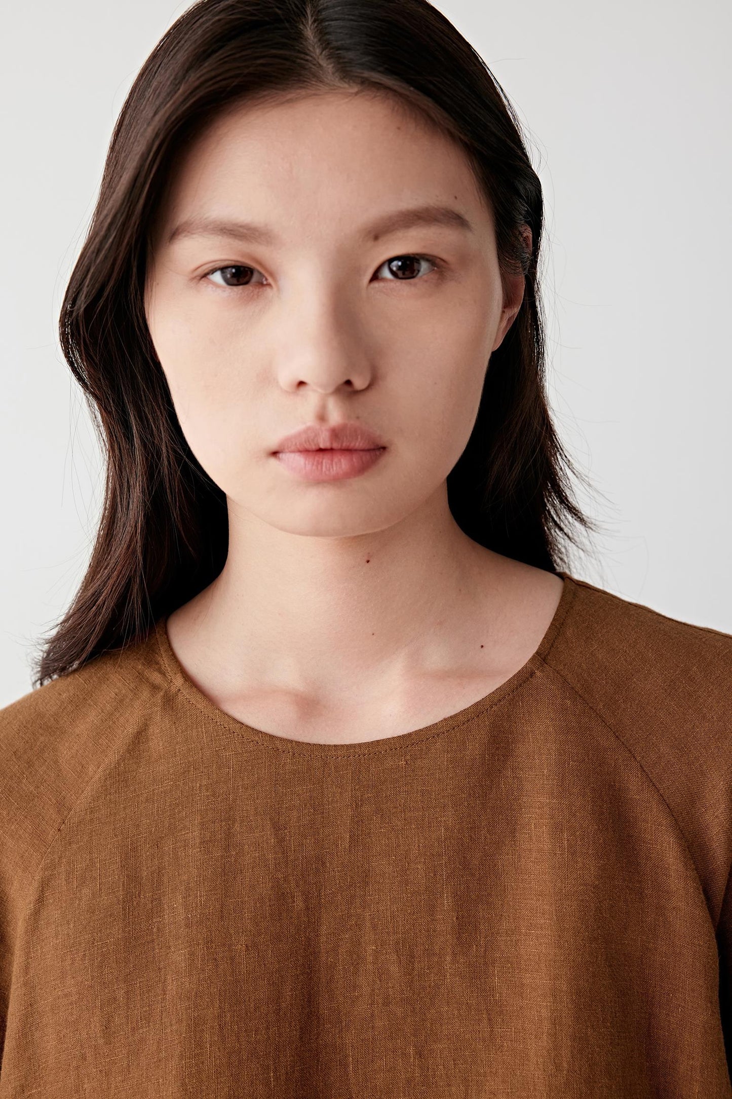 Close-up portrait focusing on the round neckline and upper body, detailing the soft texture, subtle tonal depth and lightweight woven structure of the linen surface