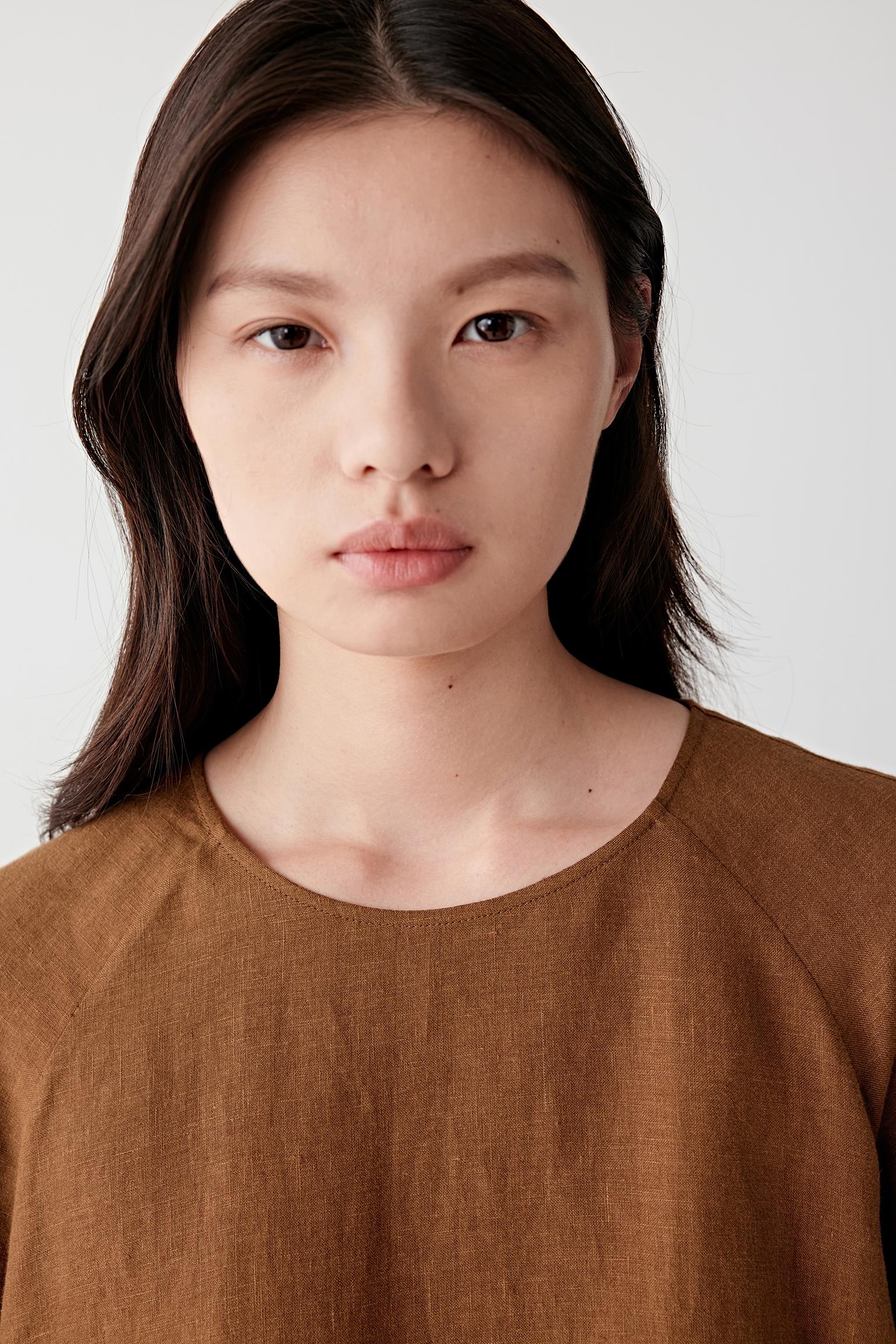 Close-up portrait focusing on the round neckline and upper body, detailing the soft texture, subtle tonal depth and lightweight woven structure of the linen surface