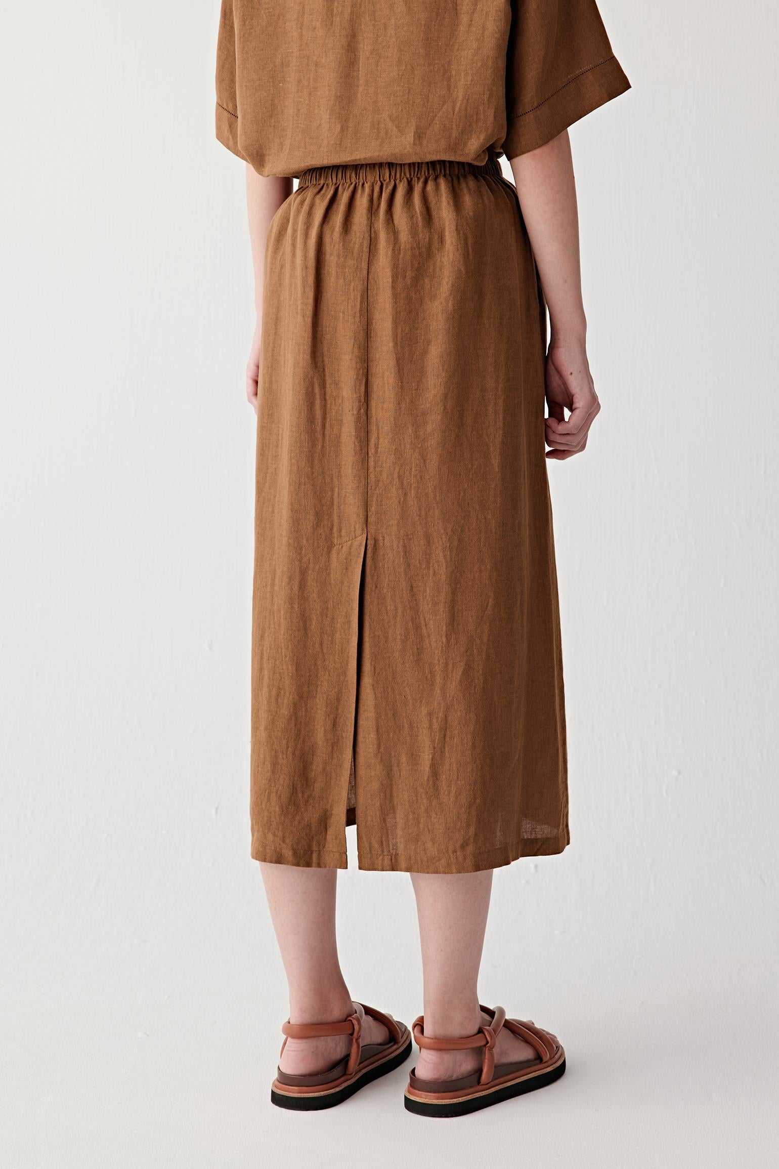 Mid-length back or three-quarter rear view showing the fluid movement and elongated shape of the skirt, with the lightweight linen construction creating soft folds and natural texture throughout the surface
