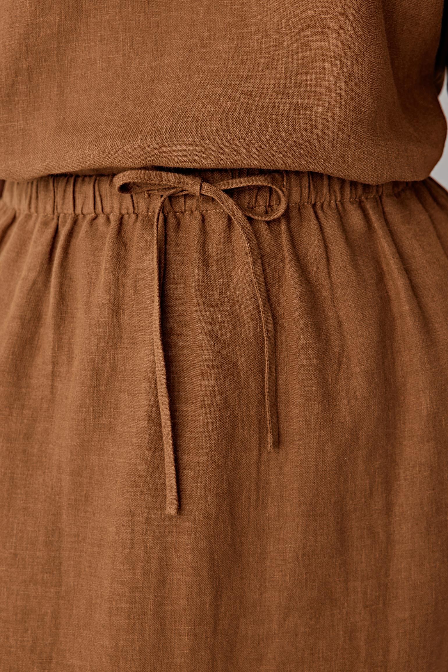 Close-up of the waistband and drawstring detailing the gathered construction, visible stitching and dry textured weave characteristic of plain-woven linen in a warm brown tone