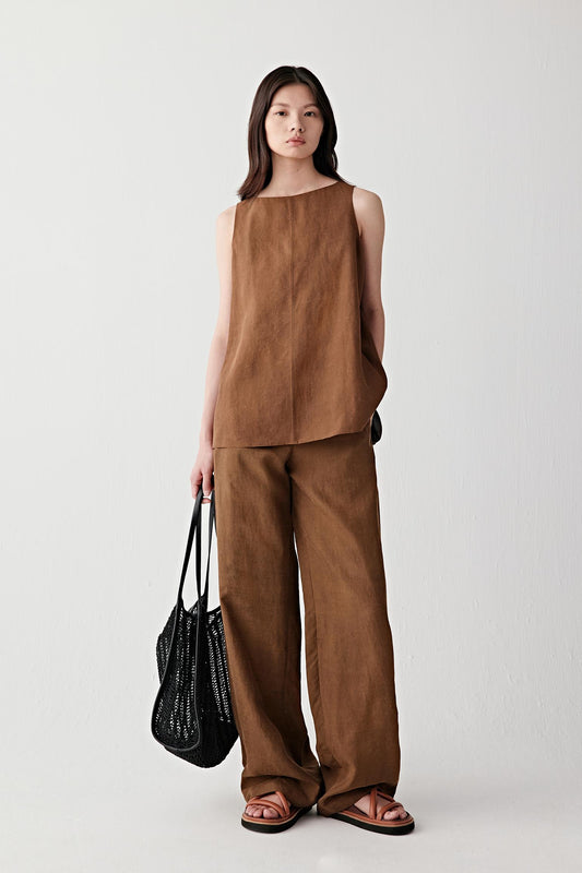 Full-length front view of a woman wearing deep clay-brown trousers in Gambiered Canton Gauze, highlighting the fluid drape, matte surface and subtle tonal depth developed through the traditional dyeing process