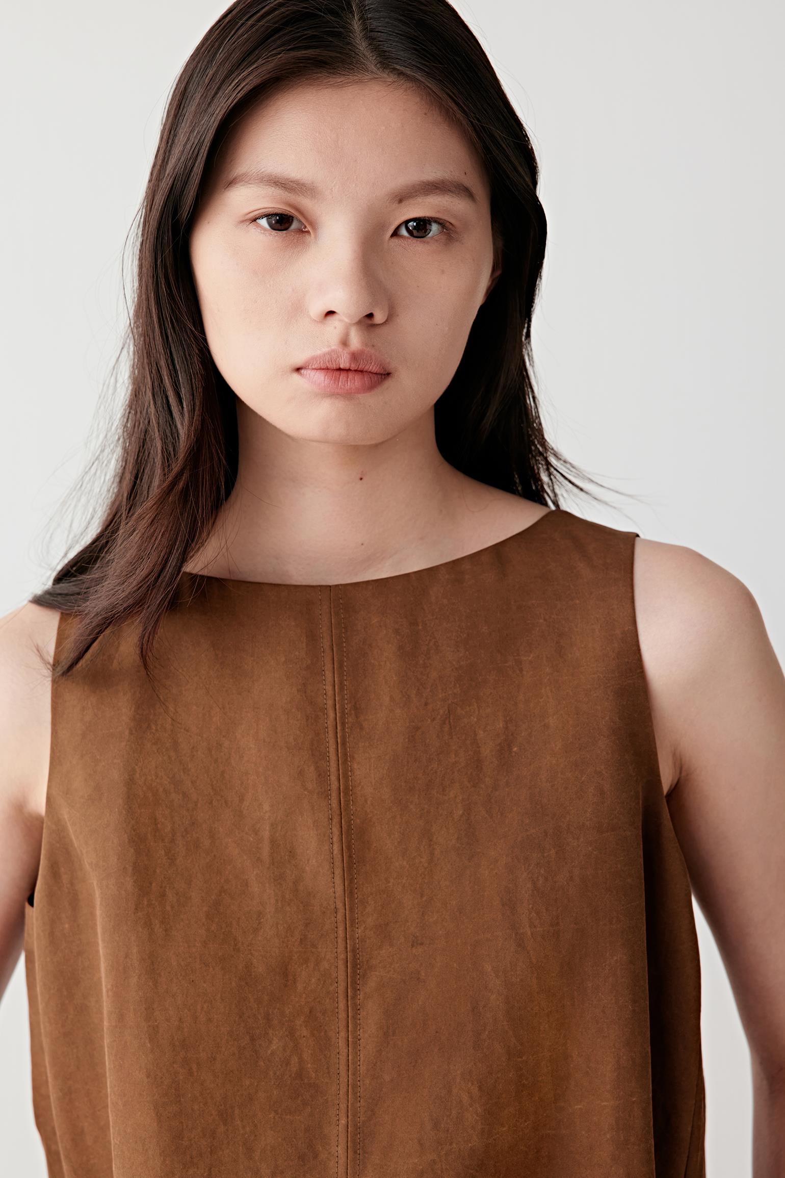Close-up portrait focusing on the round neckline and upper body, detailing the compact woven texture, matte finish and subtle tonal variation within the warm brown surface