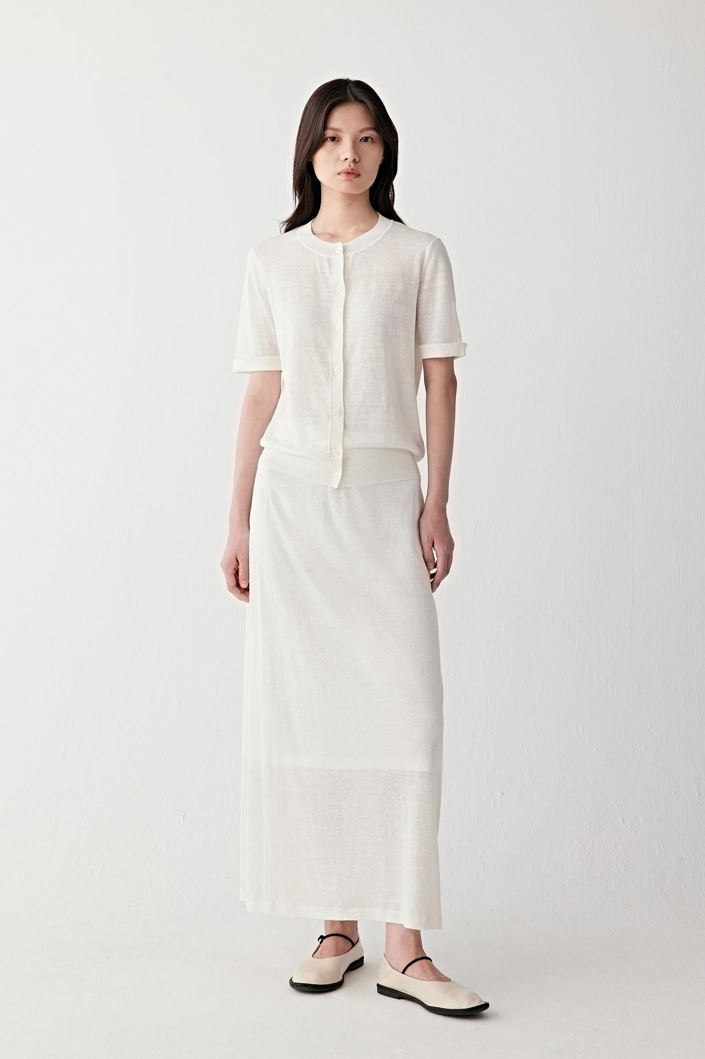 Full-length front view of a woman wearing an off-white linen and nylon skirt paired with a matching top, highlighting the straight silhouette, fluid drape and lightly textured woven surface with subtle semi-sheer depth