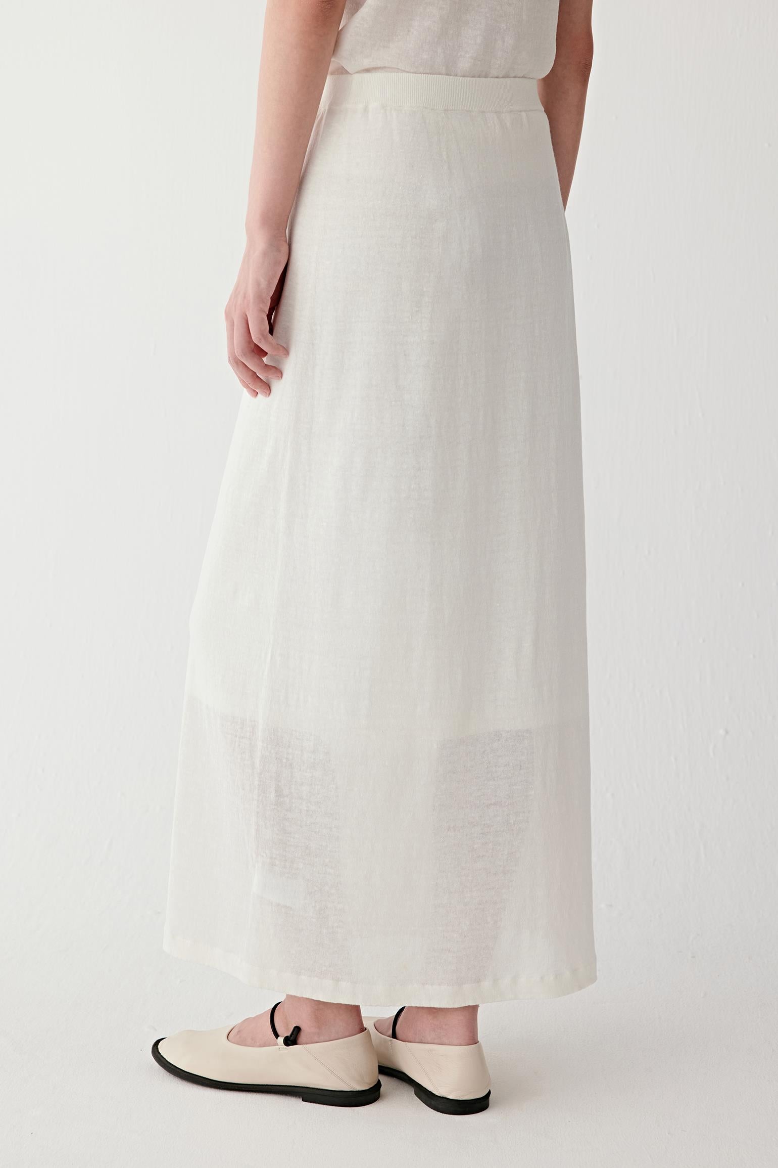 Side or three-quarter back view showing the fluid drape and continuous vertical line of the skirt, with the lightweight fabric moving softly around the body
