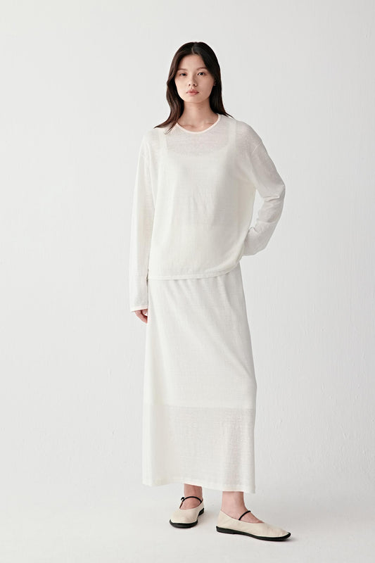 Full-length front view of a woman wearing an off-white pullover in linen and nylon, highlighting the lightweight knit structure, fluid drape and subtly sheer surface