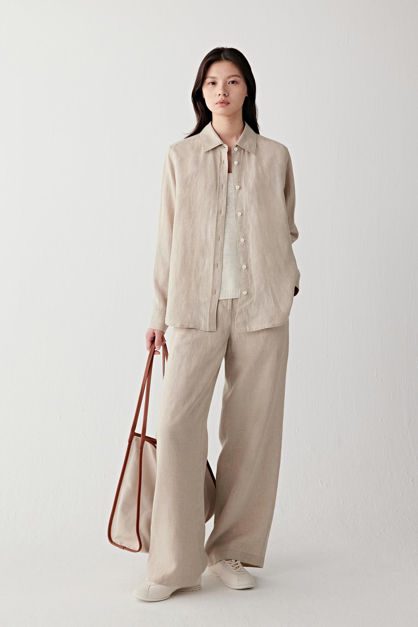 Full-length front view showing the shirt paired with matching trousers, emphasizing the curved hem, relaxed fit and natural movement of the linen fabric