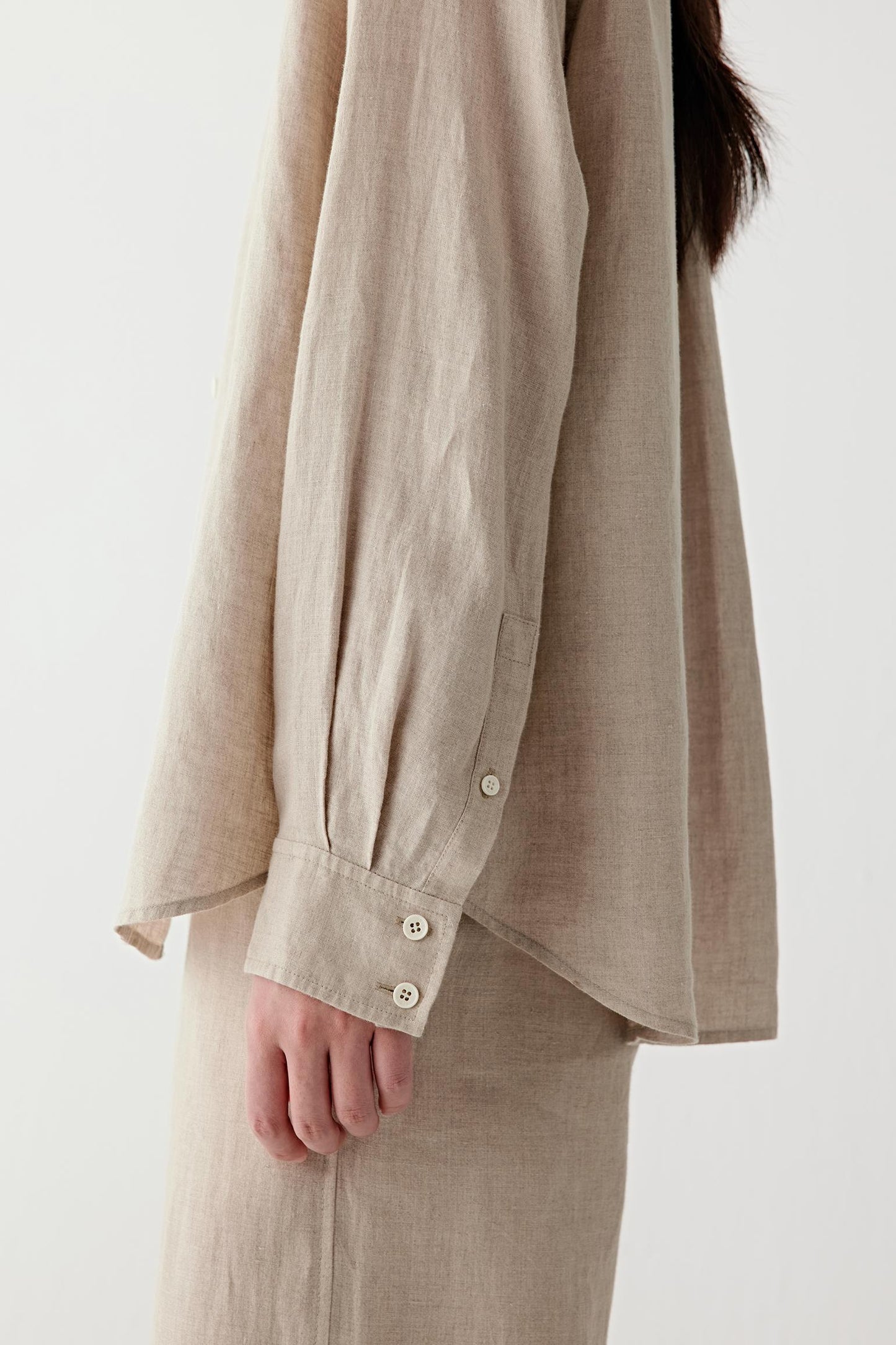 Close-up of cuff and fabric surface showing the buttoned cuff construction, visible stitching and subtle irregularities characteristic of plain-woven linen