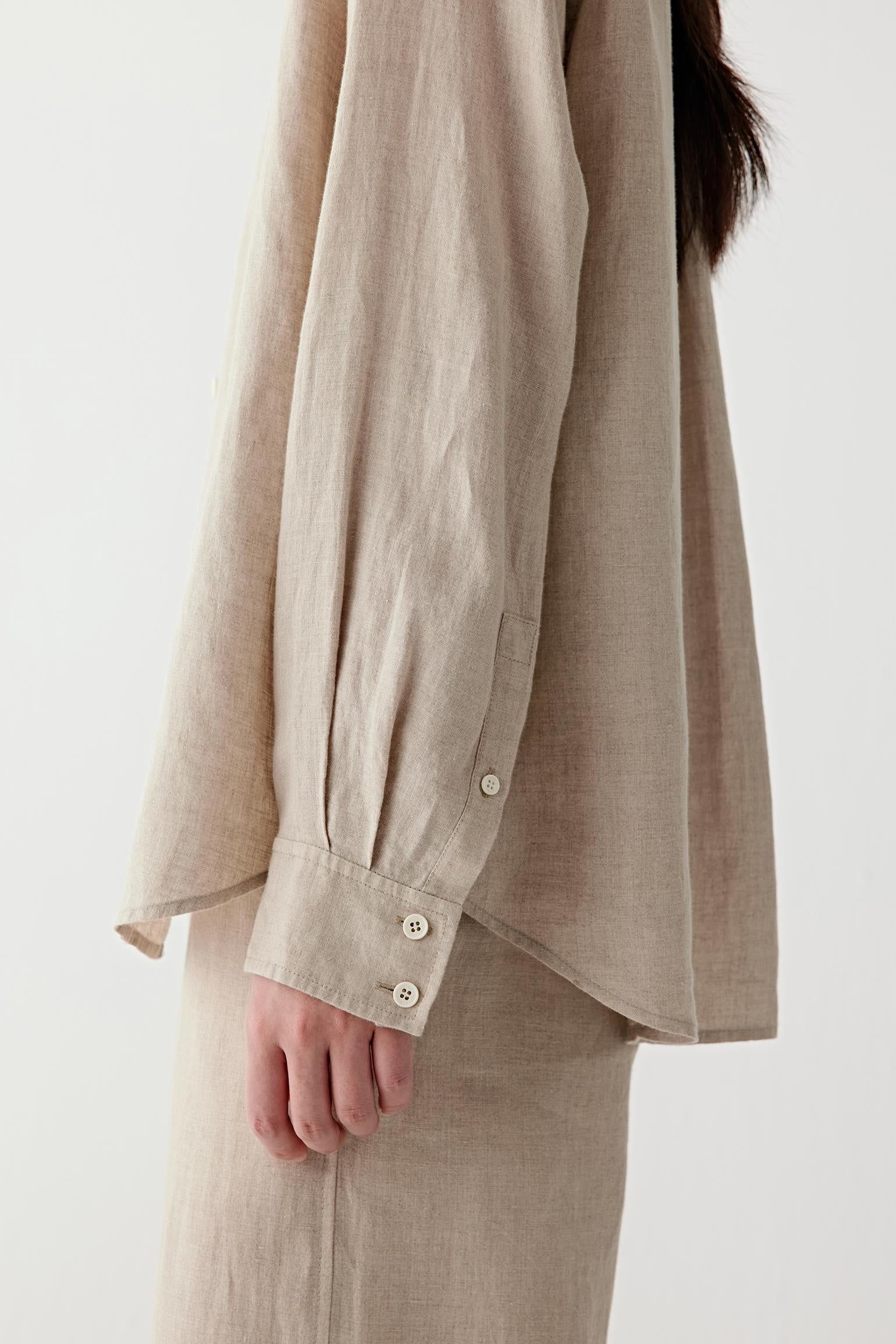 Close-up of cuff and fabric surface showing the buttoned cuff construction, visible stitching and subtle irregularities characteristic of plain-woven linen