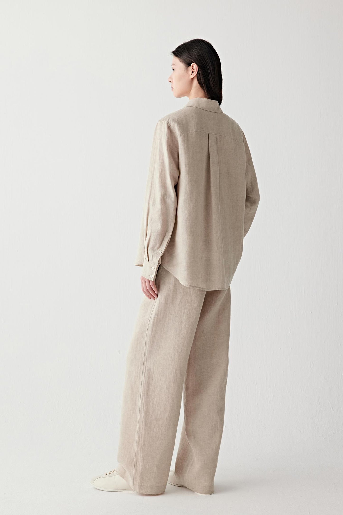 Side or back view highlighting the long sleeves, back pleat and fluid drape through the silhouette