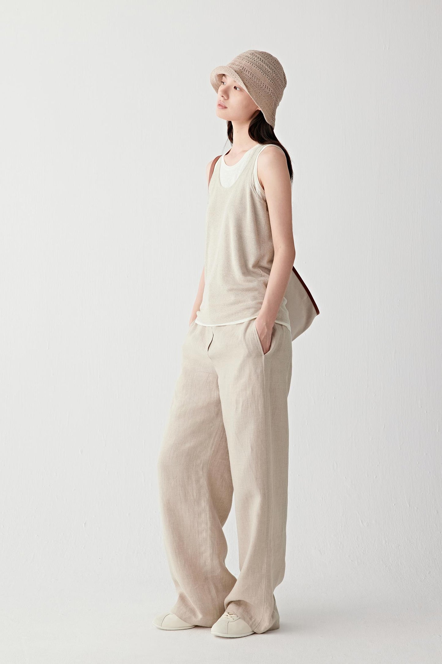 Full-length front view of a woman wearing beige trousers in plain-woven linen, highlighting the lightweight structure, fluid drape and softly textured matte surface