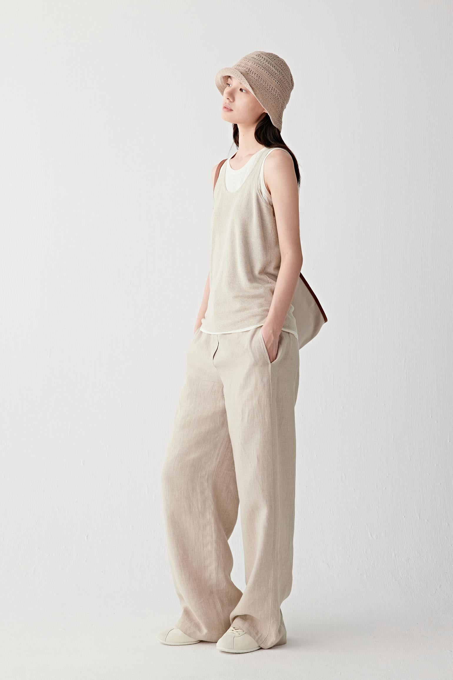 Full-length front view of a woman wearing beige trousers in plain-woven linen, highlighting the lightweight structure, fluid drape and softly textured matte surface