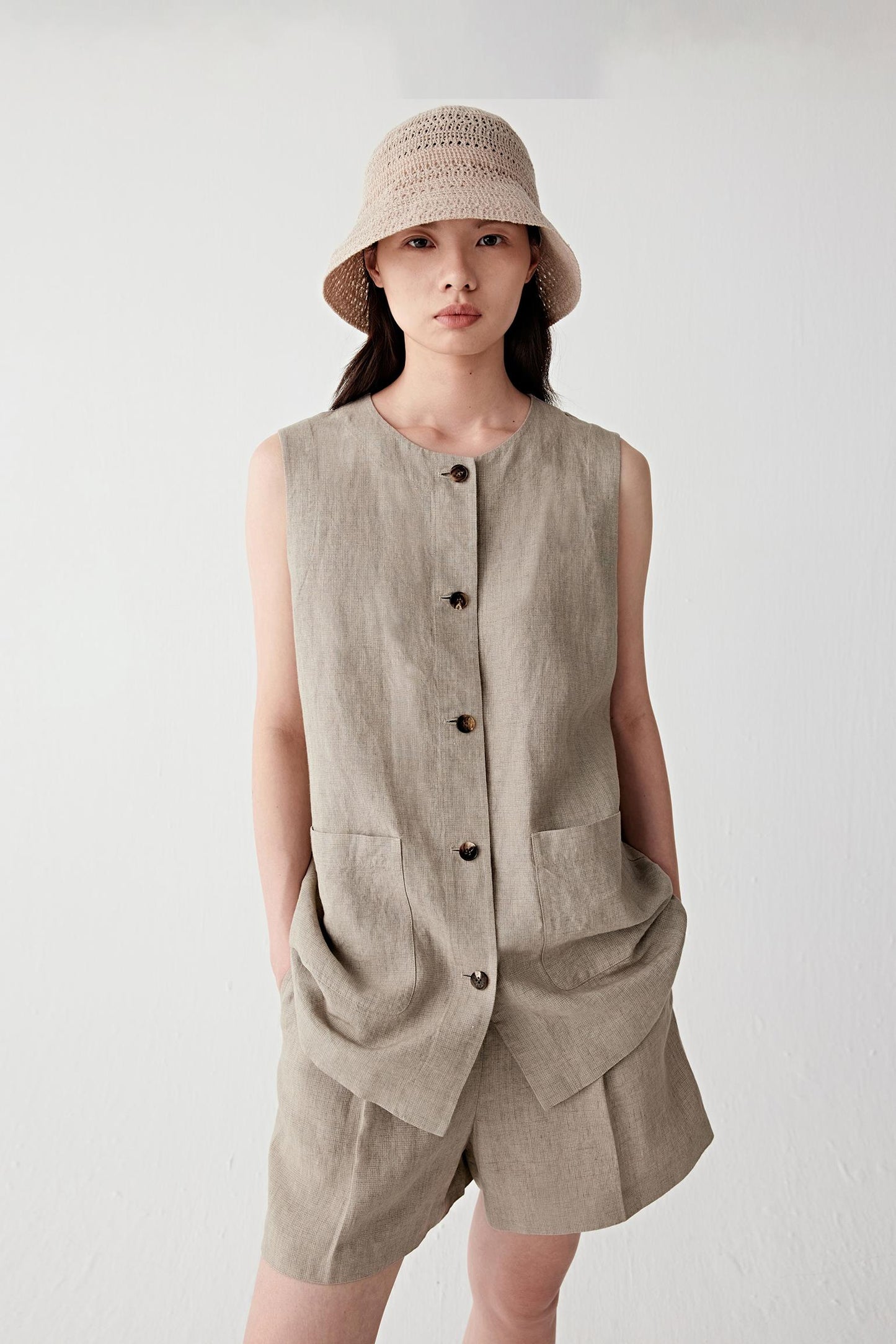 Full-length front view of a woman wearing light brown mini-check linen shorts, highlighting the lightweight woven structure, subtle check pattern and softly textured matte surface