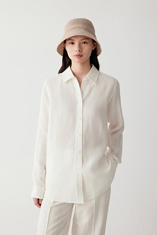 Full-length front view of a woman wearing a light cream linen shirt with a relaxed silhouette, highlighting the lightweight woven structure, fluid drape and softly irregular linen surface