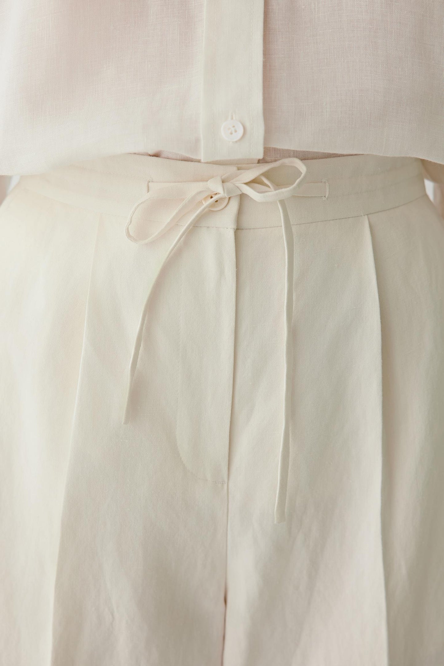 Close-up of waistband and front pleats detailing the drawstring waistband, pleated construction and softly textured undyed surface with visible stitching and natural depth