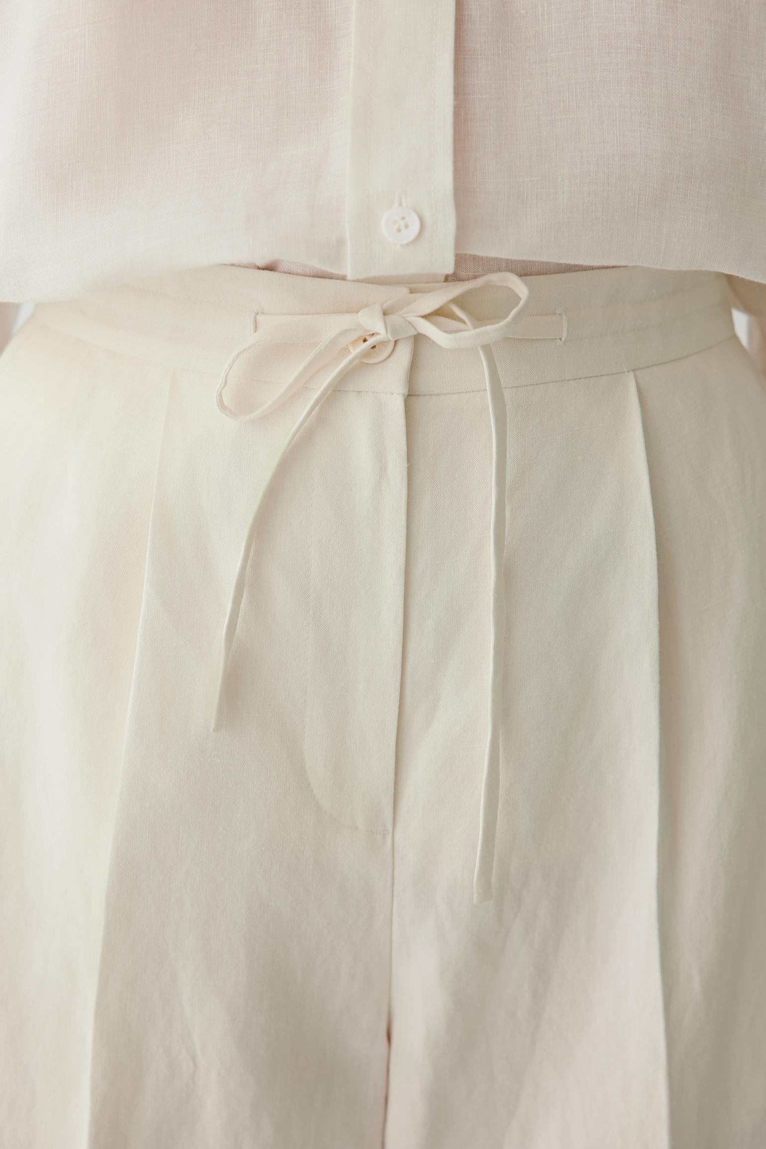 Close-up of waistband and front pleats detailing the drawstring waistband, pleated construction and softly textured undyed surface with visible stitching and natural depth