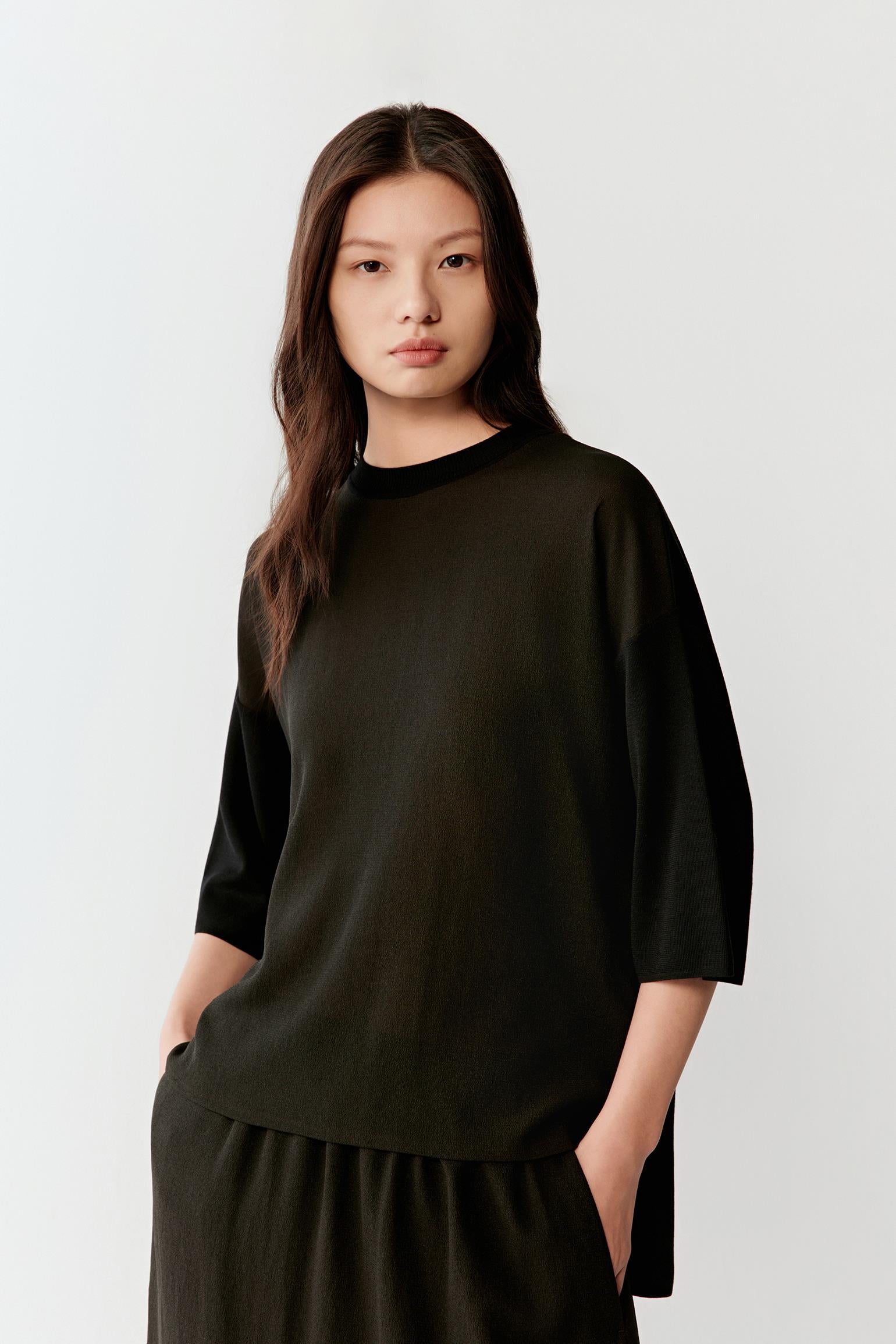 Front view of a woman wearing a deep black silk pullover with three-quarter sleeves, highlighting the smooth fine jersey construction, fluid drape and softly flowing silhouette