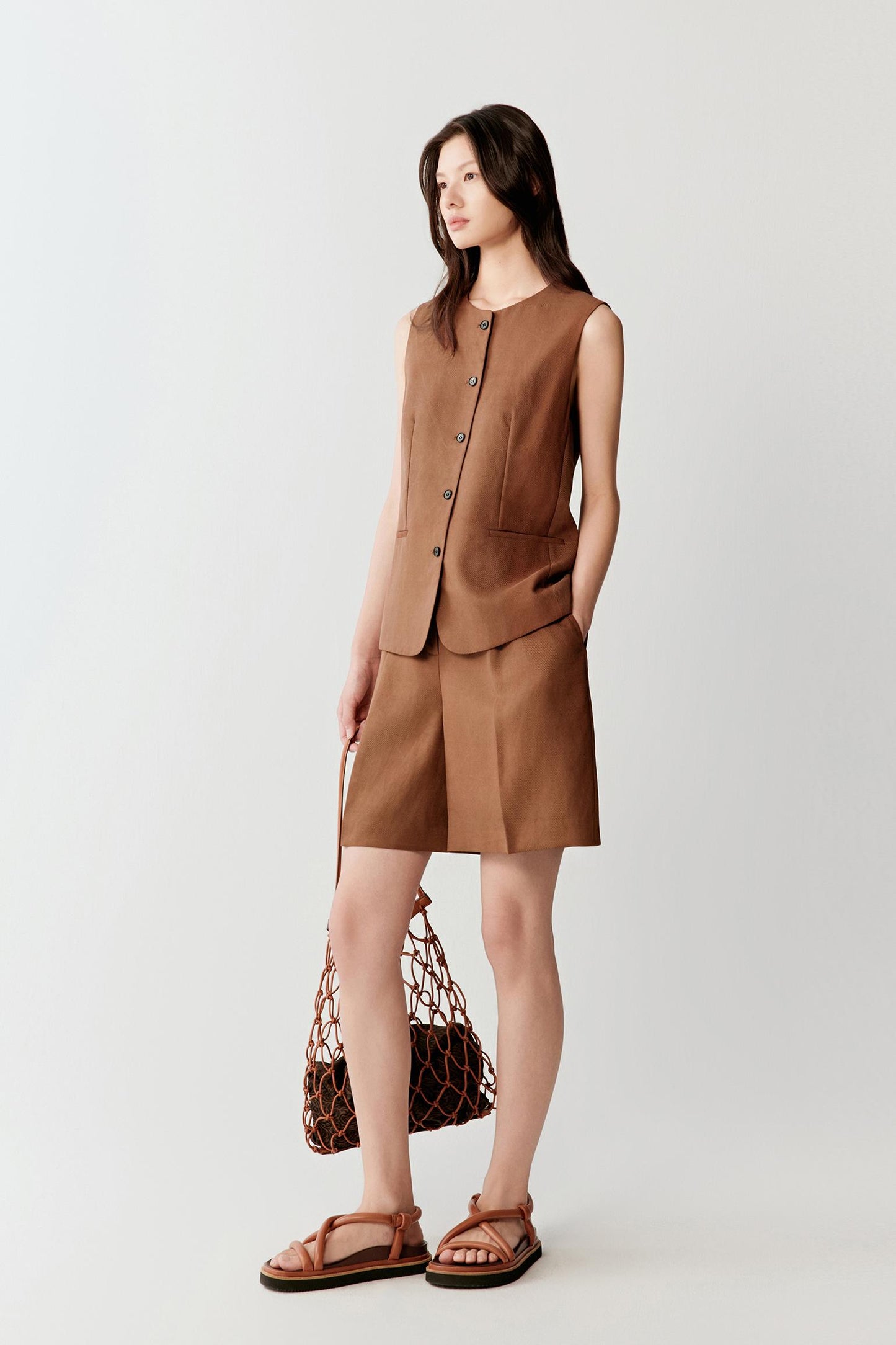 Full-length front view showing the vest paired with matching shorts, emphasizing the elongated silhouette, front button fastening and lightly structured shape with subtle tonal depth throughout the warm brown fabric